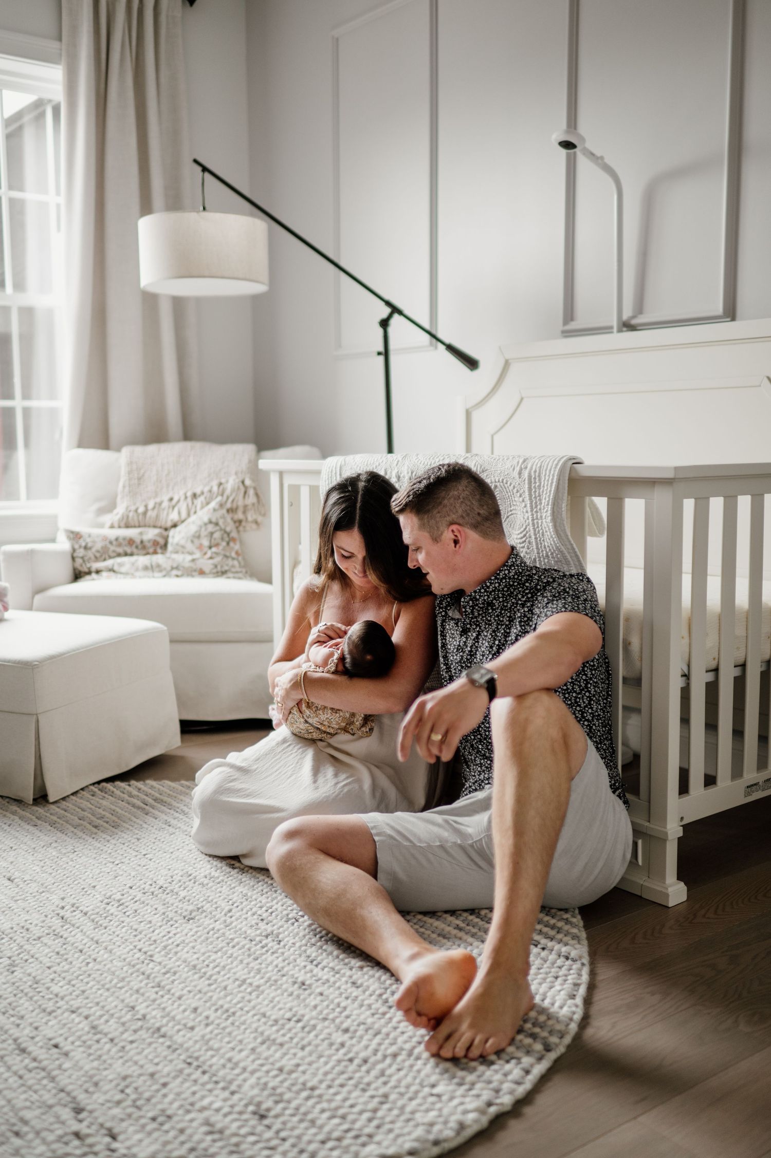 Modern nursery interior with couple sitting on round rug admiring their newborn.