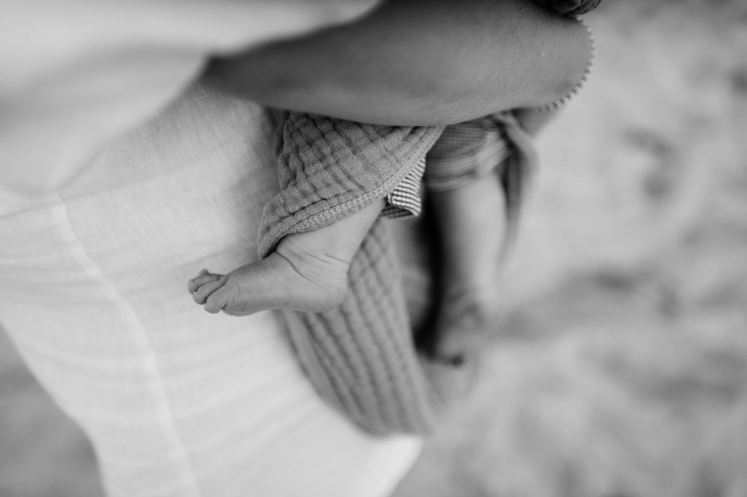 Close up black and white image of tiny baby feet being held against soft fabric.
