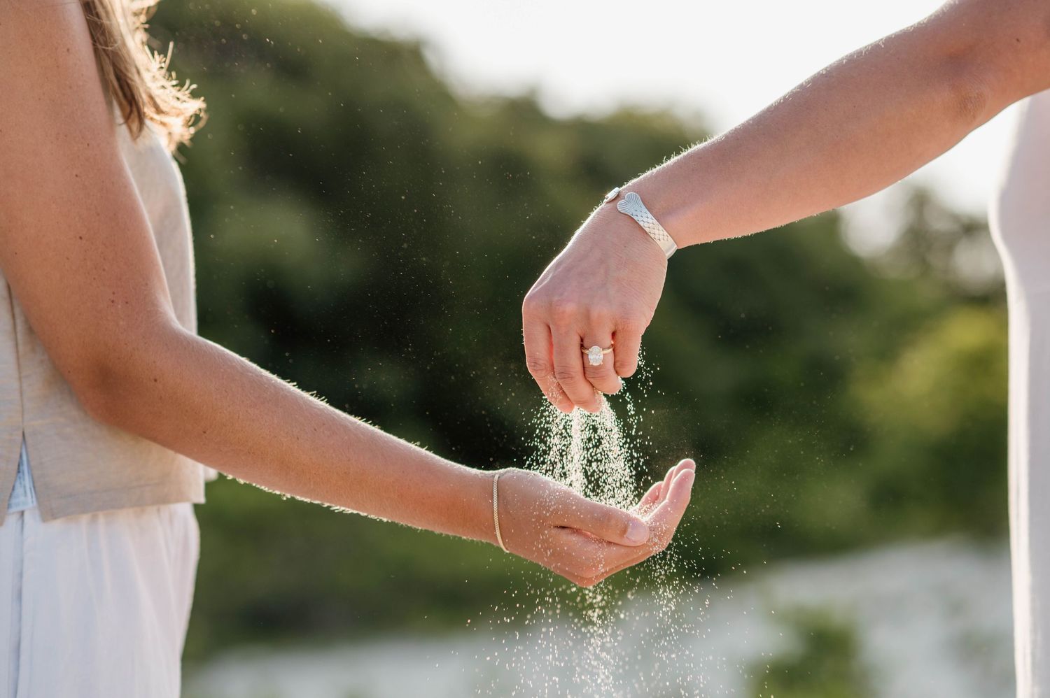 Hands sprinkling sand or glitter against a bright outdoor background.