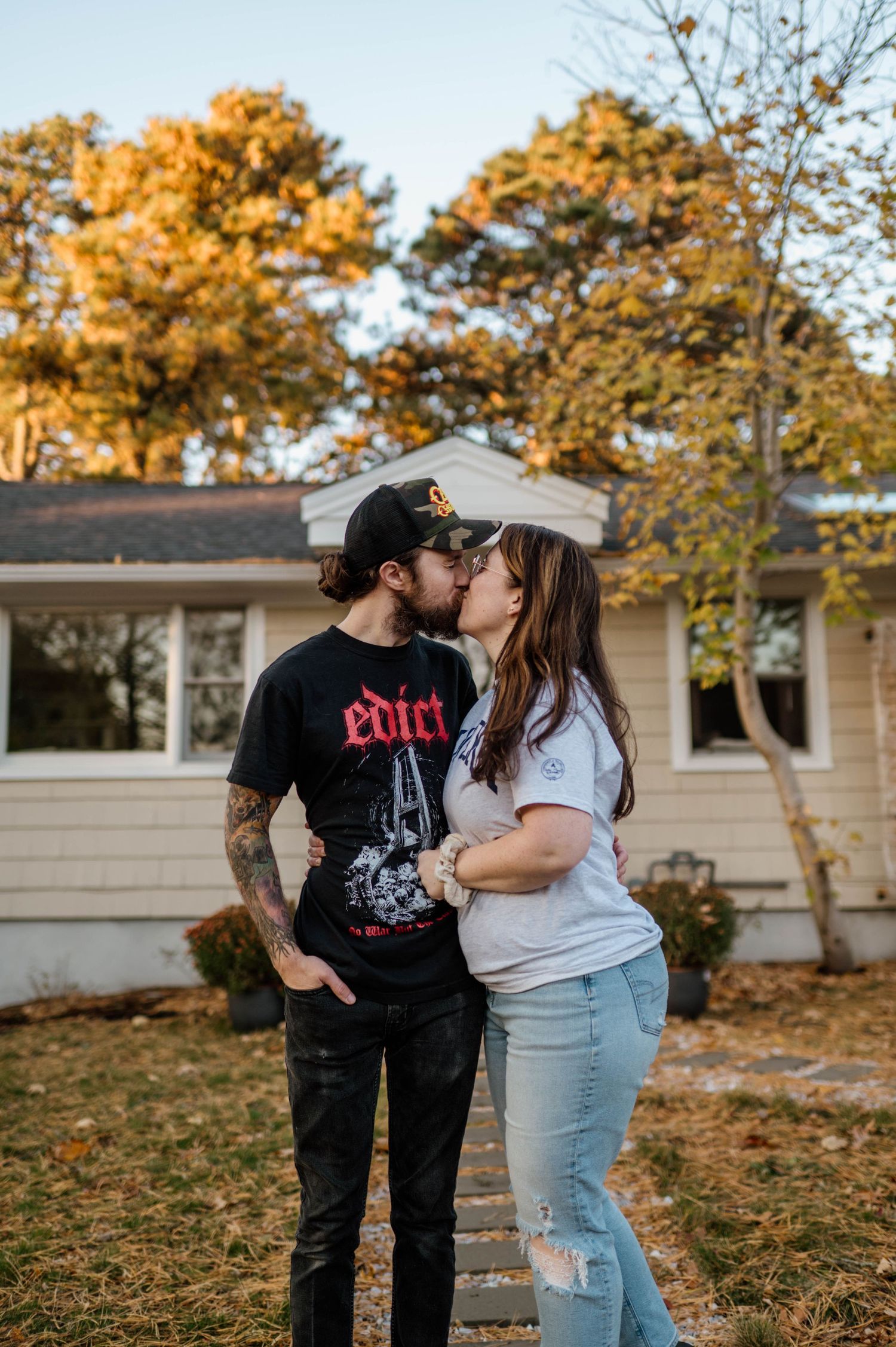 A couple in casual attire sharing a romantic moment outdoors during golden hour with autumn trees in the background.