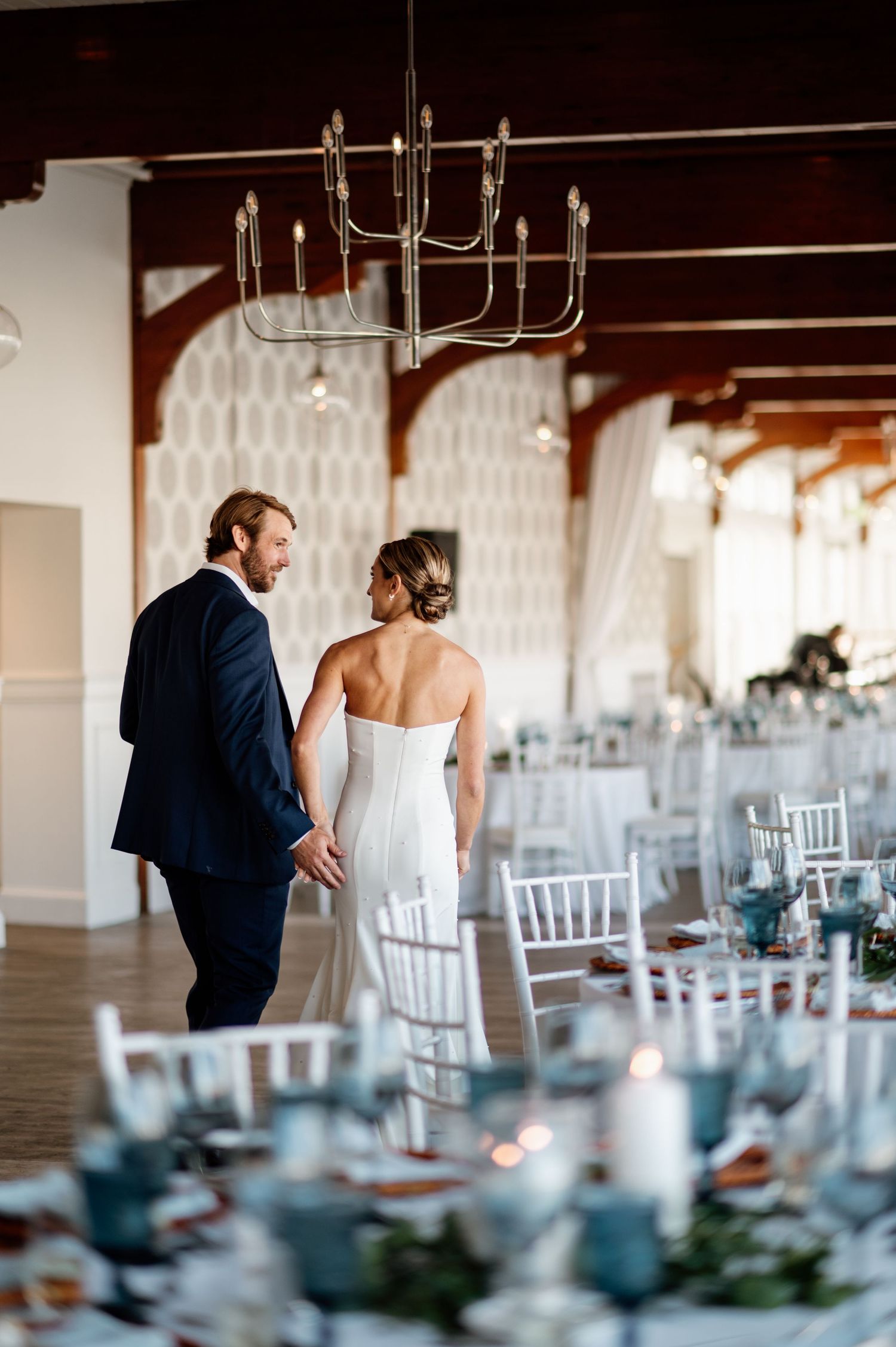 Couple shares intimate moment in elegant reception venue with chandelier and place settings.