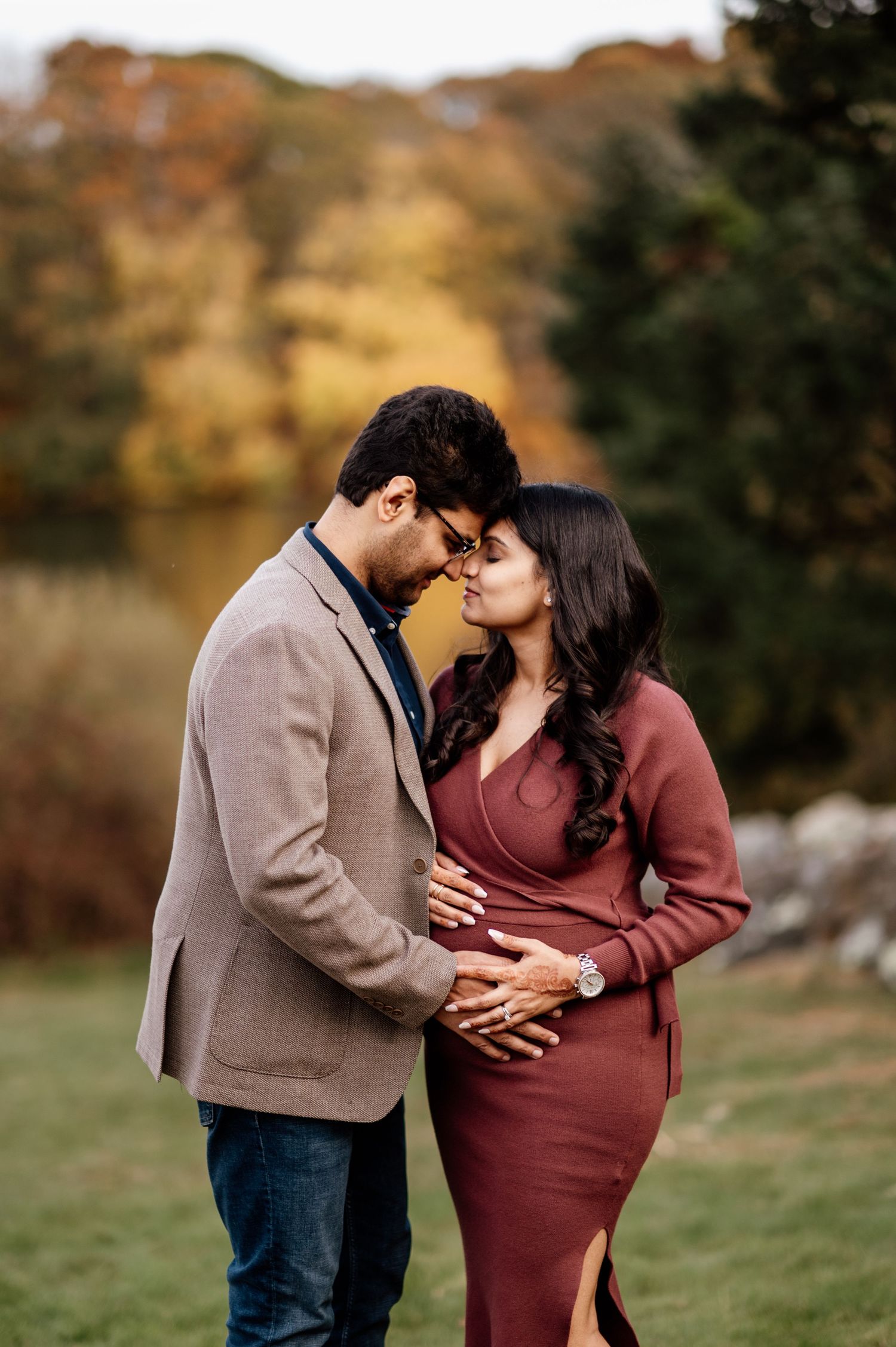 A couple in burgundy and beige sweaters share an intimate moment in a scenic autumn setting.