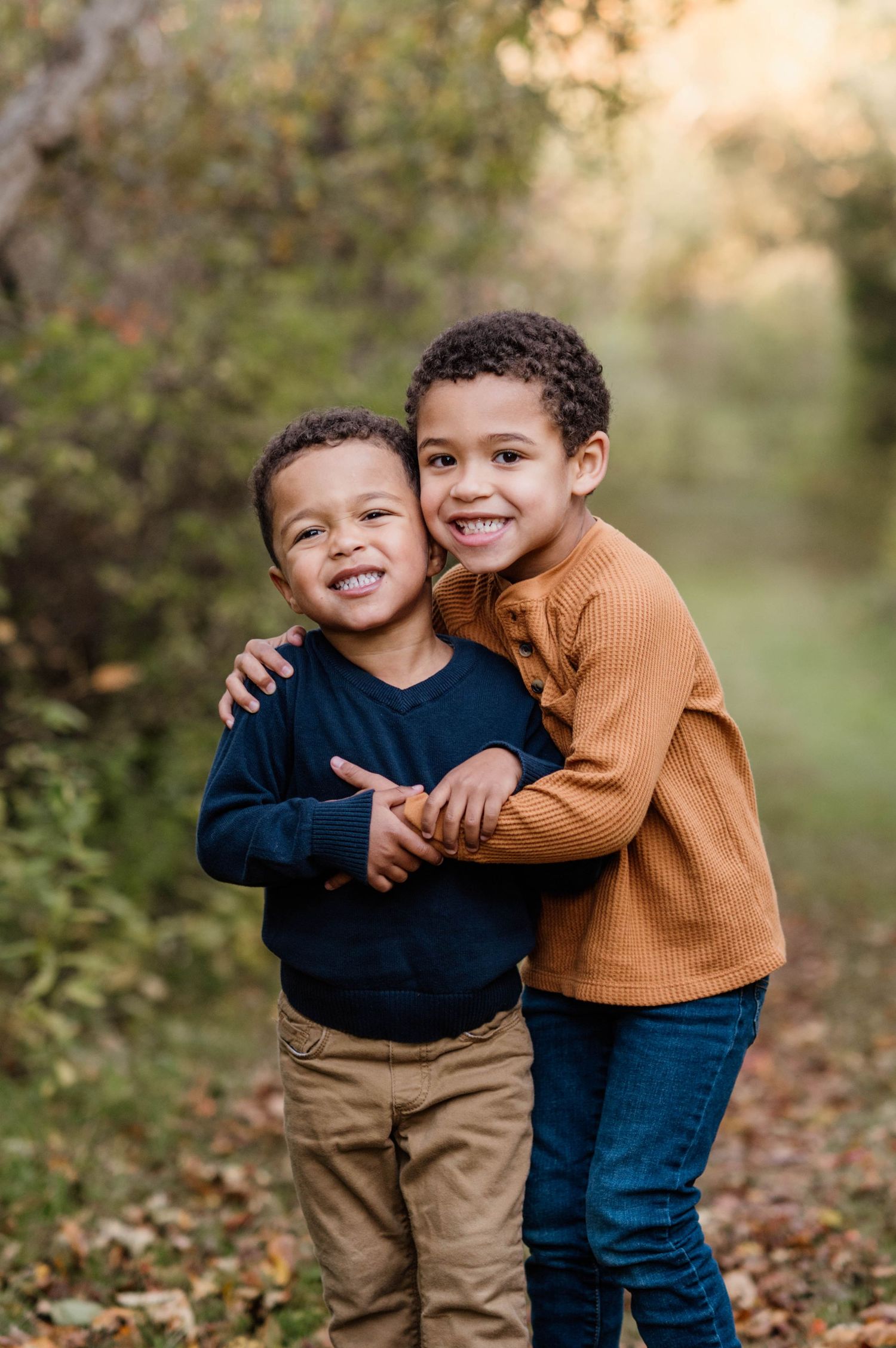 Two young children in sweaters hugging and laughing together in an autumn setting.