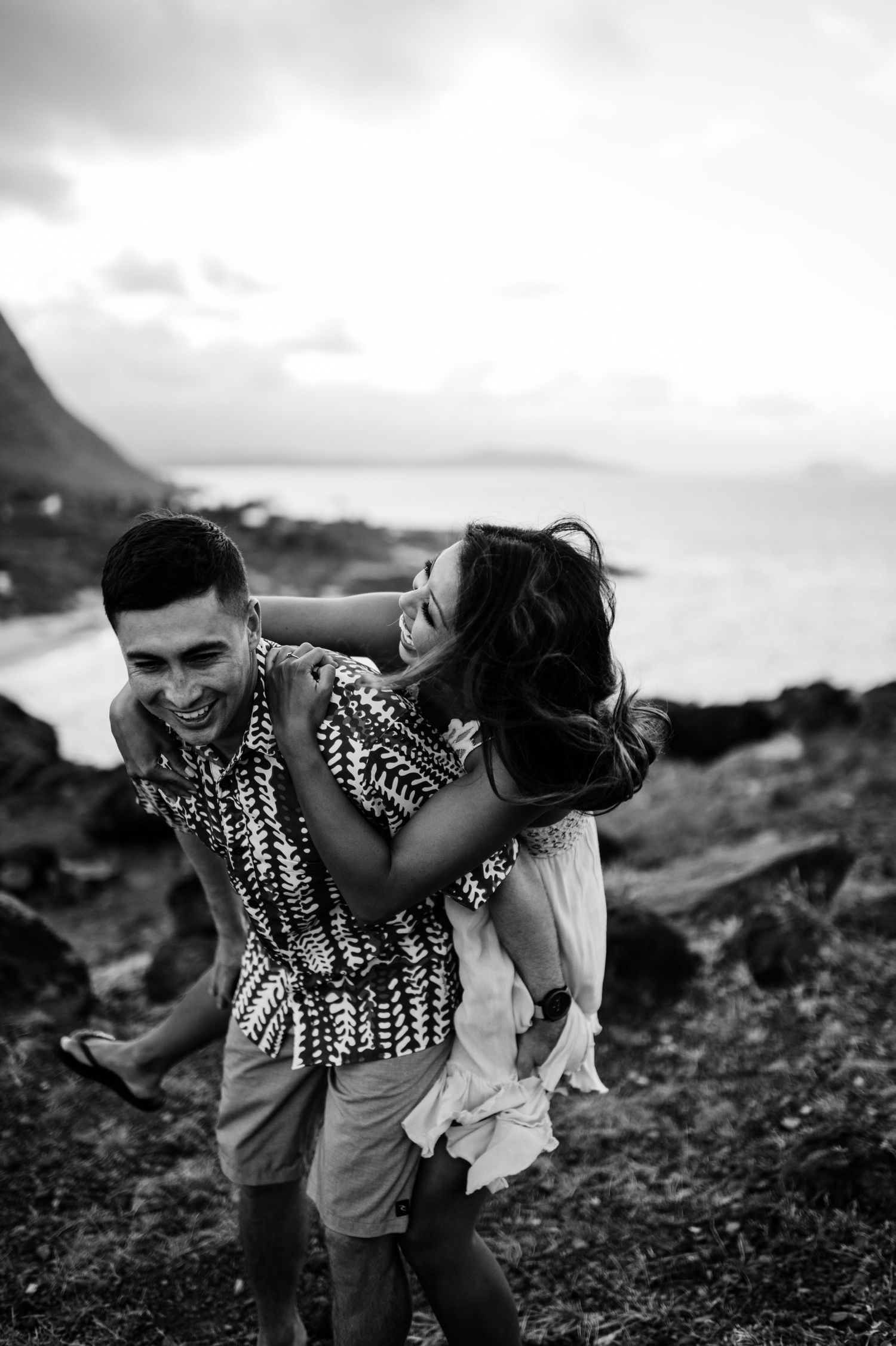 Playful couple laughing and embracing on rocky volcanic terrain at sunset.