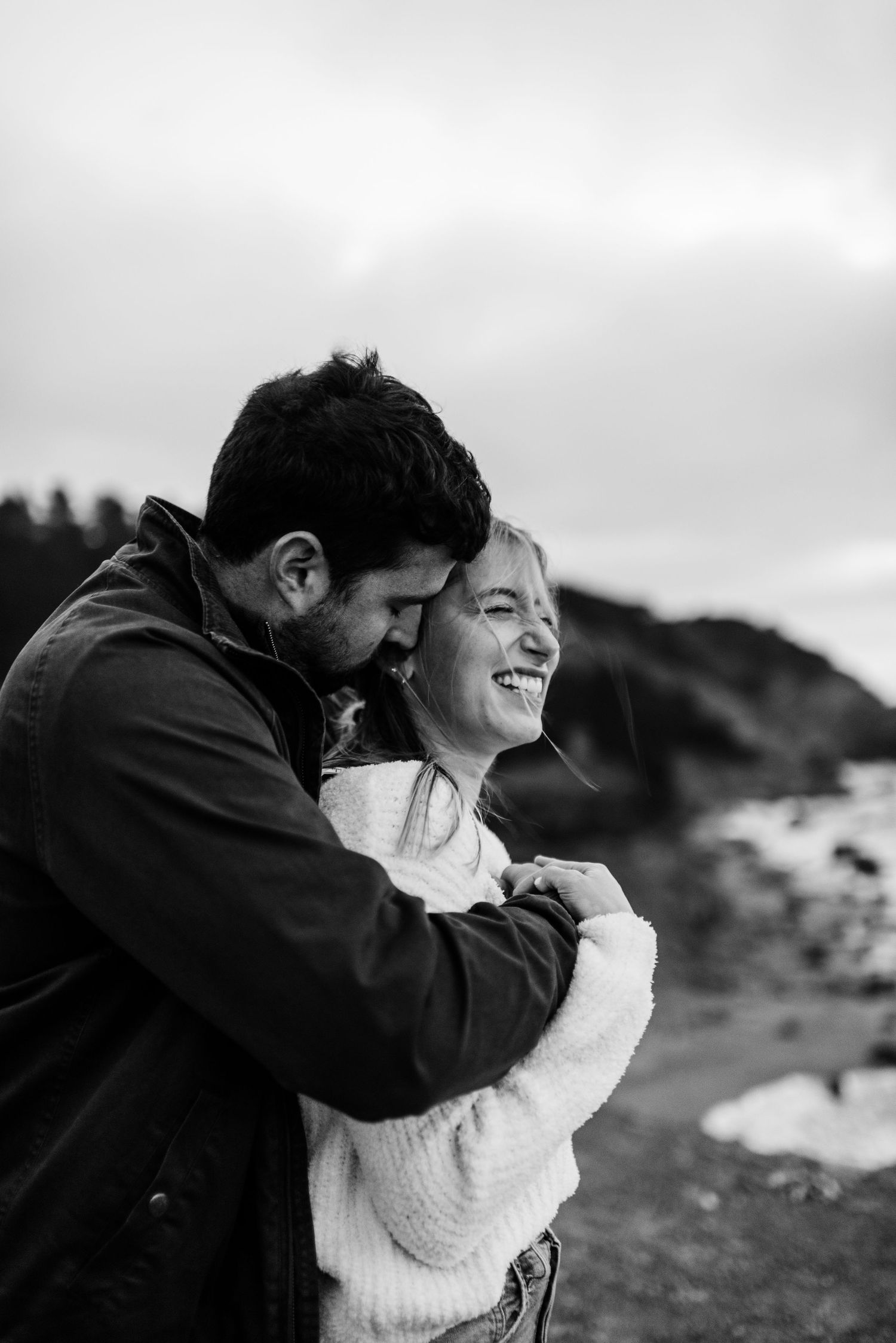 A couple shares an intimate moment against a moody sky in black and white photography.