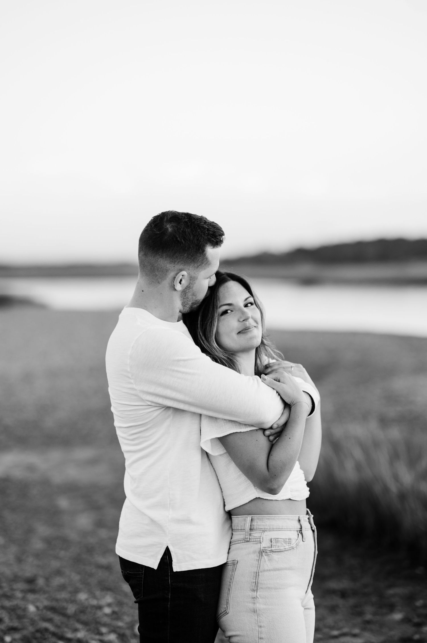 A couple embraces on a beach at sunset in black and white photography.