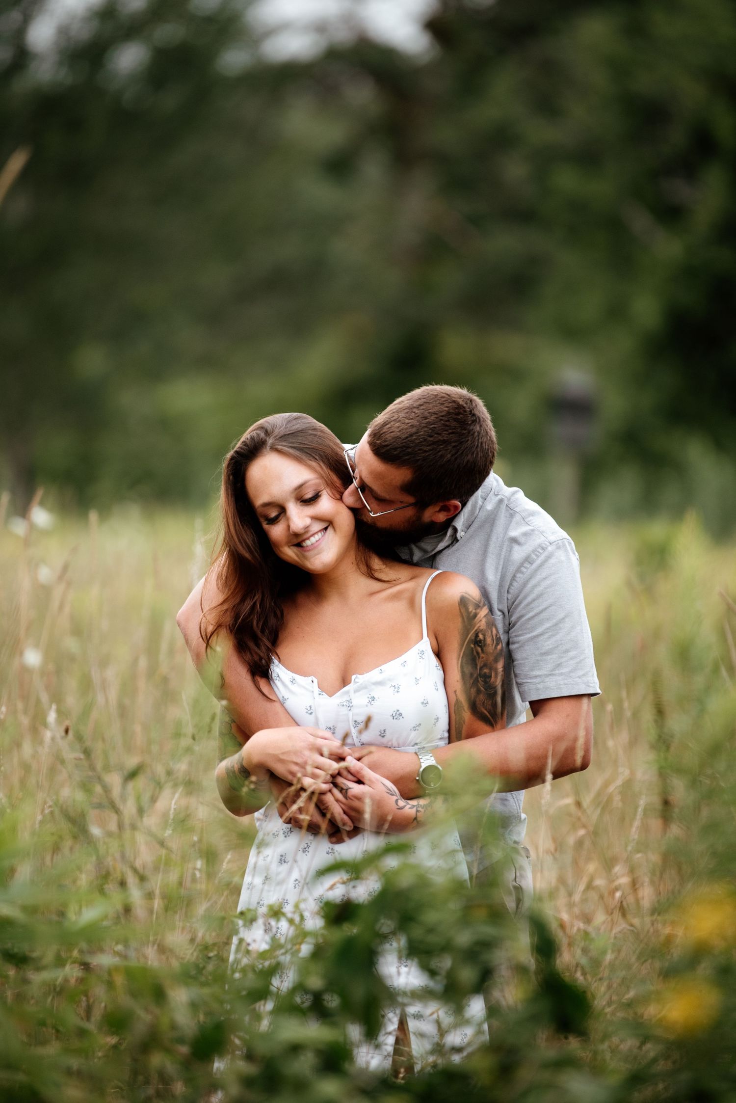 Intimate couple shares tender moments while lying in tall grass and wildflowers.