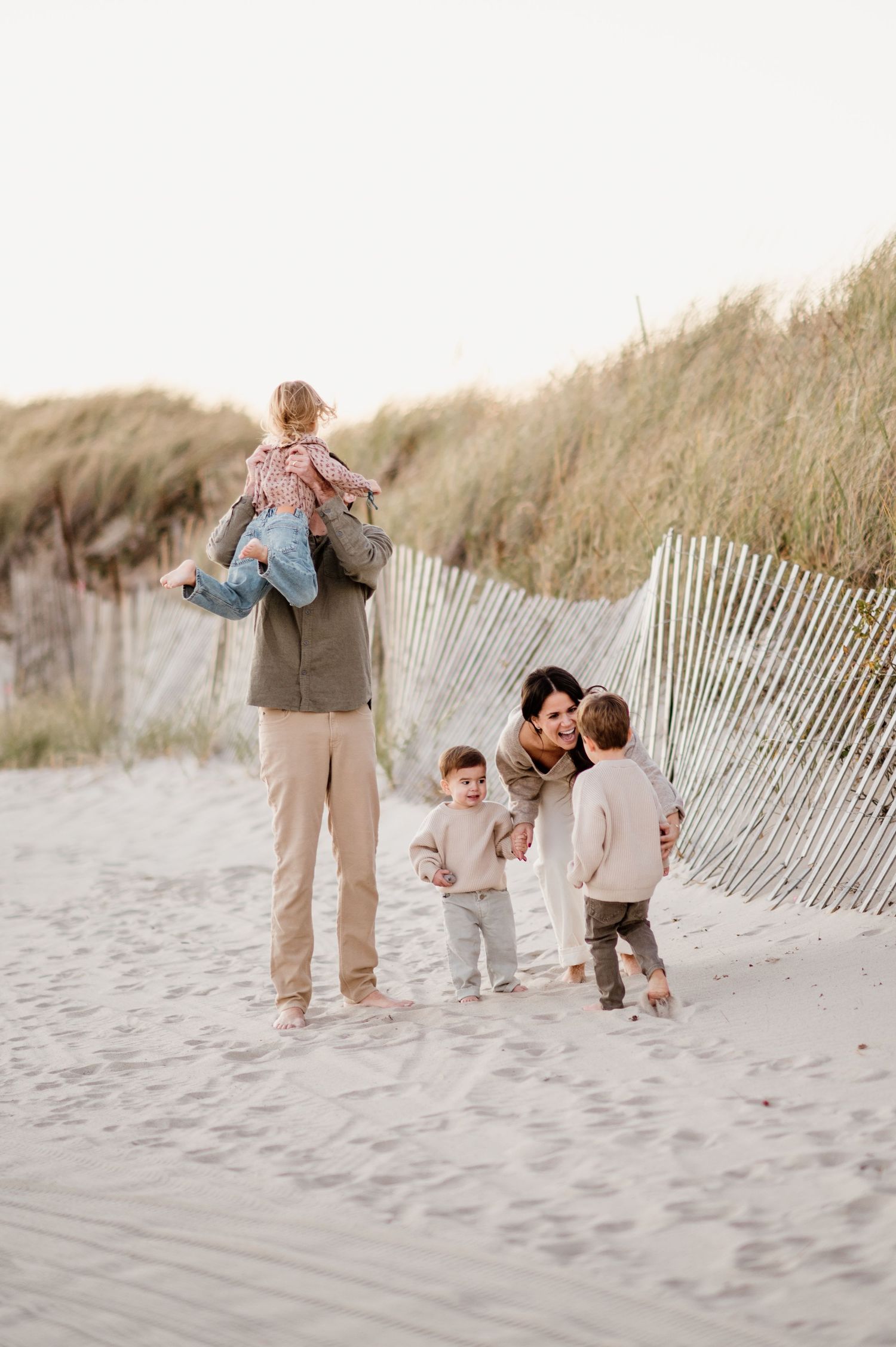 Family walking together along sandy beach dunes with wooden fence in soft evening light.
