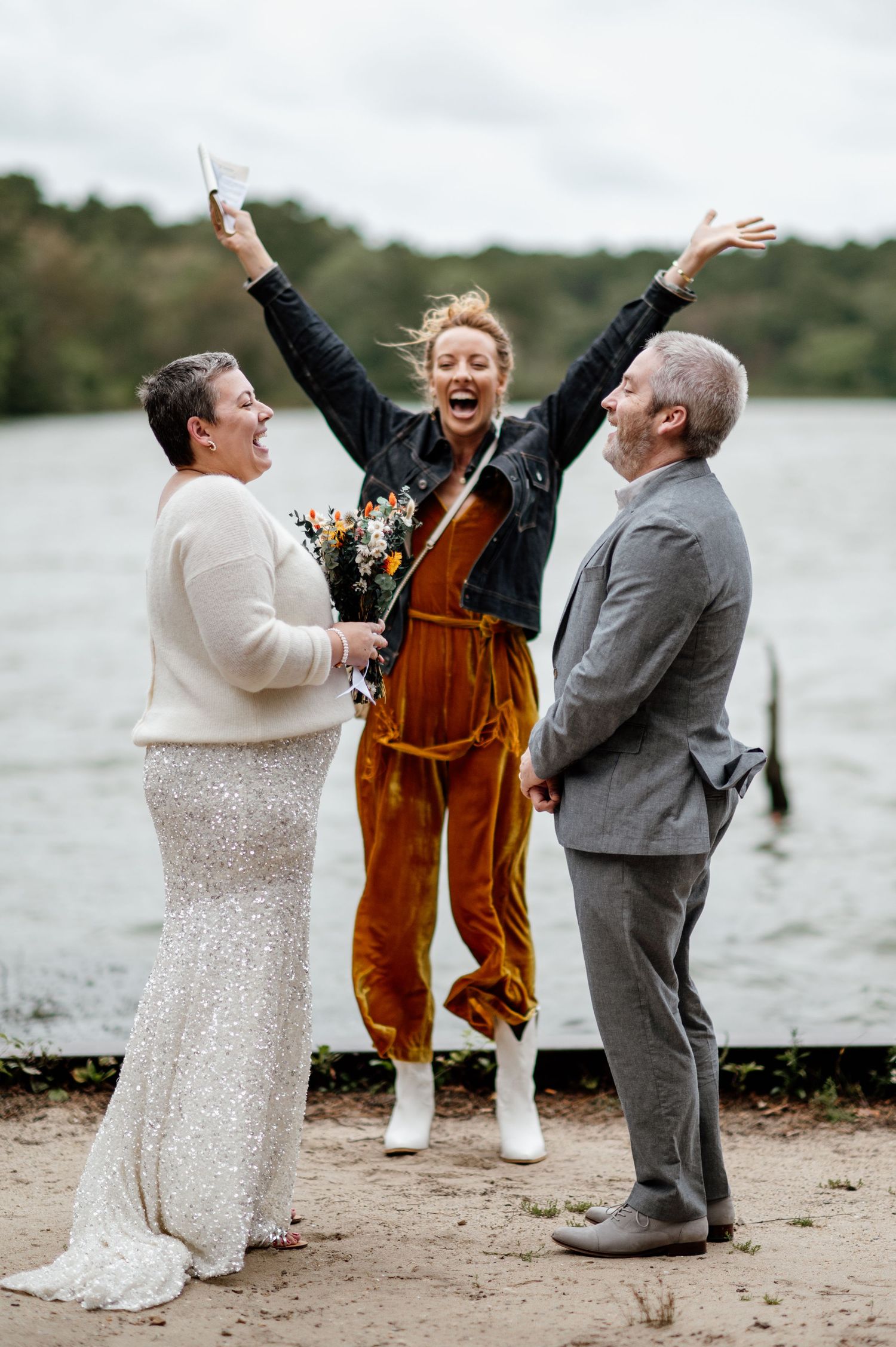 Wedding party celebrating joyfully on a beach with expressive poses and laughter.