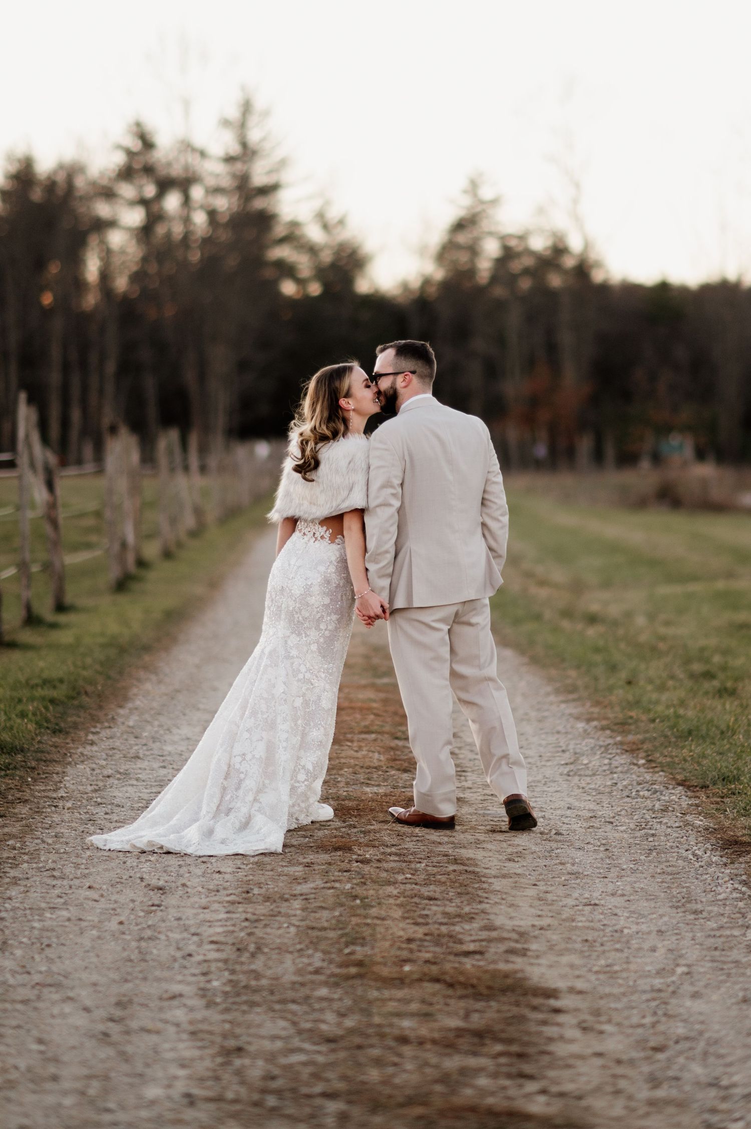 A romantic wedding couple shares intimate moments on a tree-lined path during their countryside photo session.