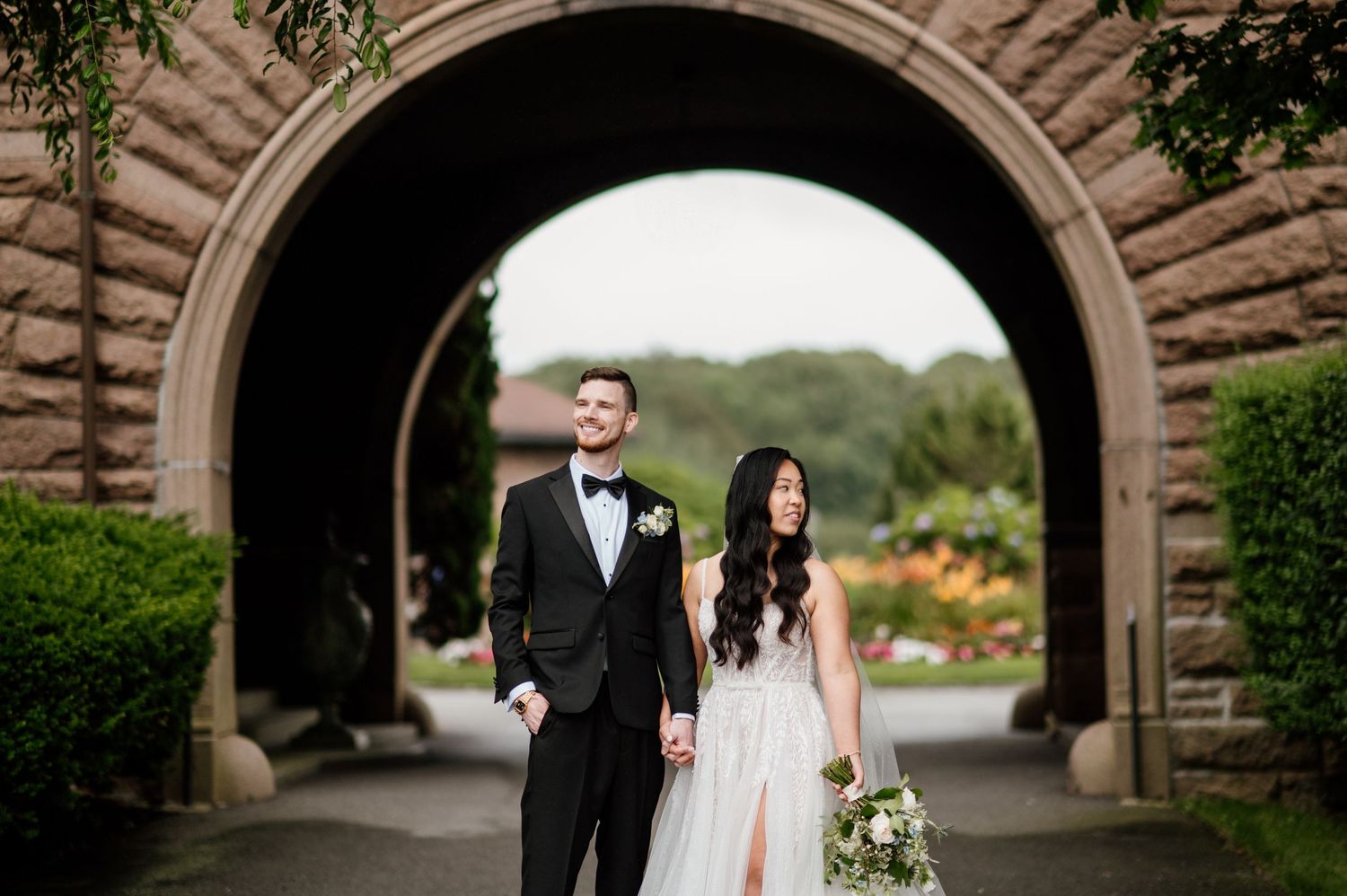 A bride and groom share a romantic moment under a stone archway surrounded by lush greenery.