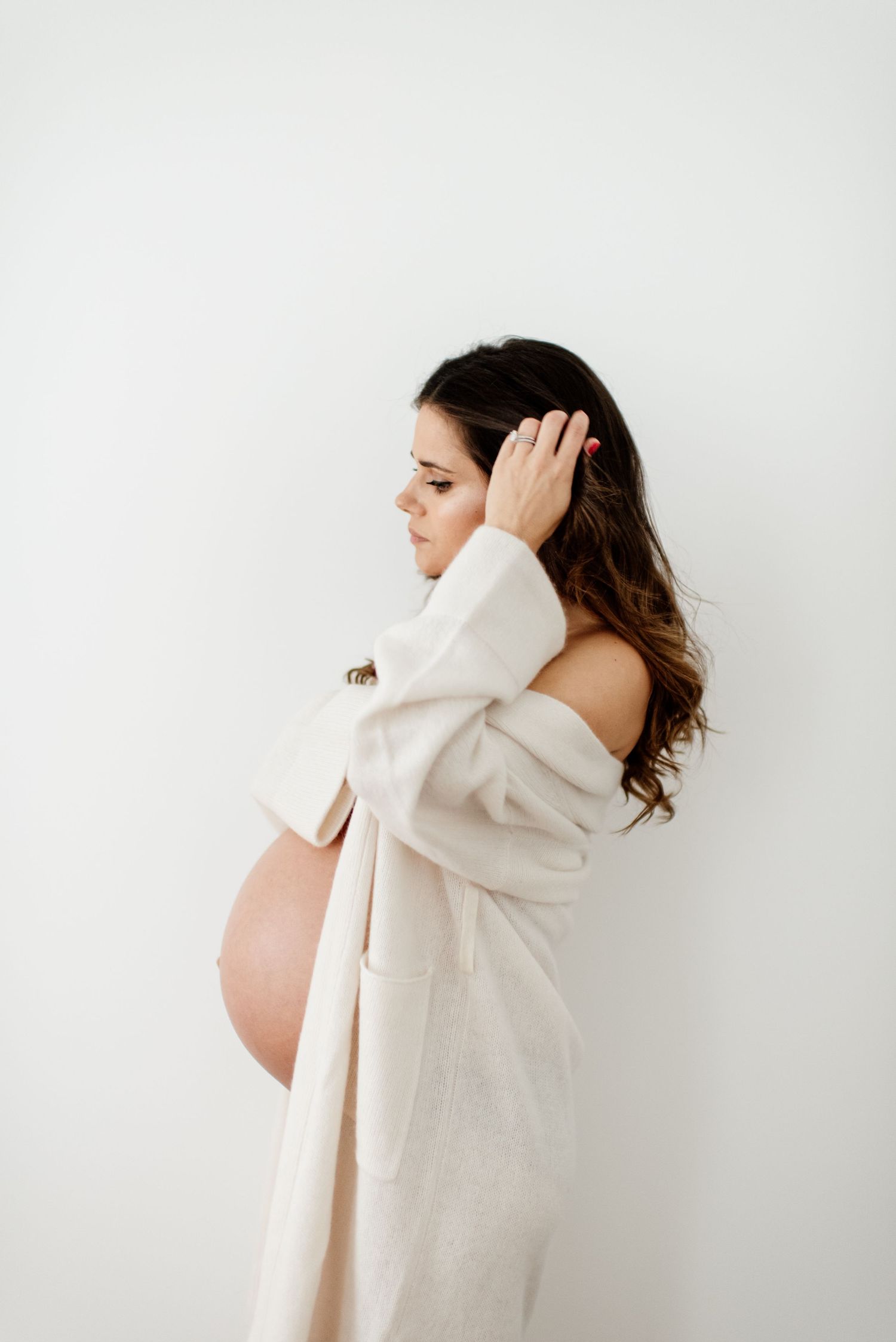 Artistic maternity photo series showing a woman in a white sweater against minimal background.