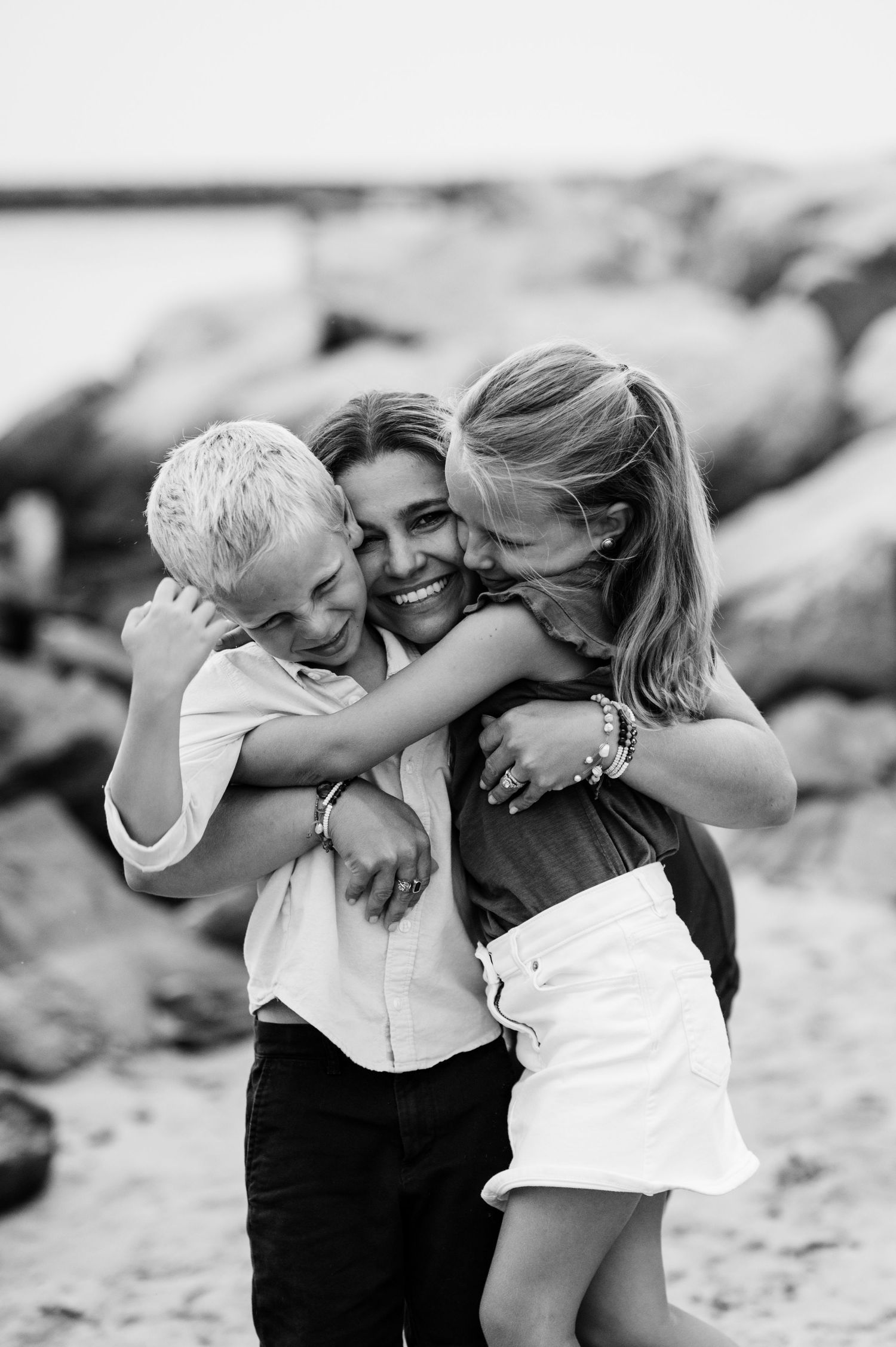 Family playing and embracing on sandy beach in black and white photography.