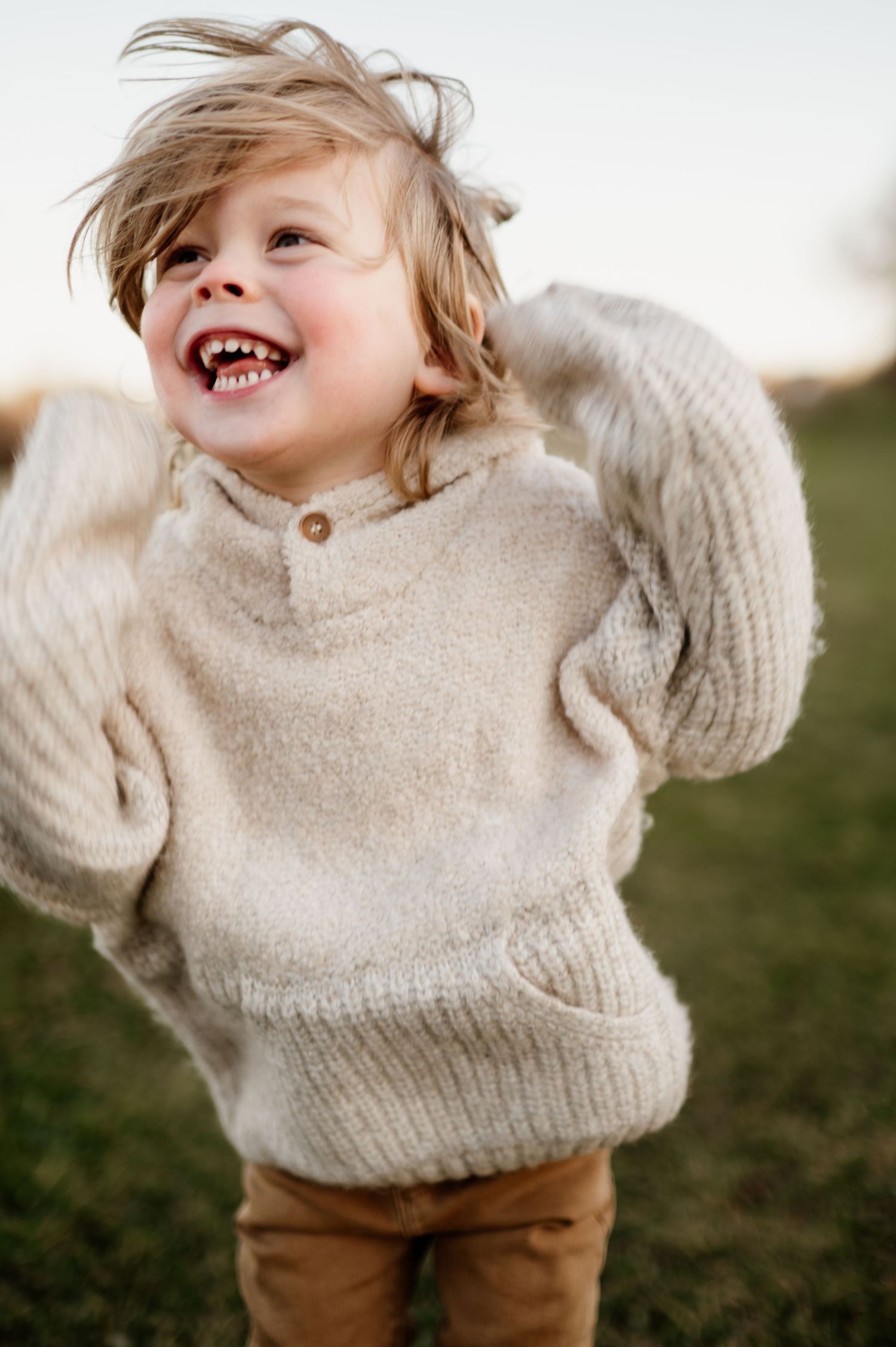 A joyful child in a cozy beige sweater laughs and plays outdoors during a golden hour photo session.