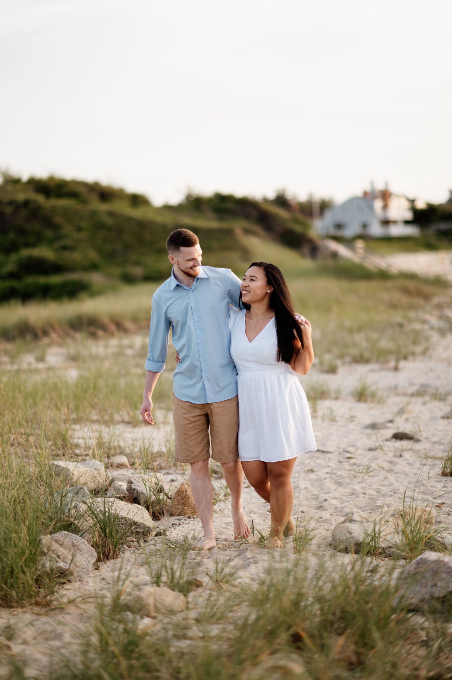 A couple takes a romantic stroll along a sandy beach path with coastal vegetation.