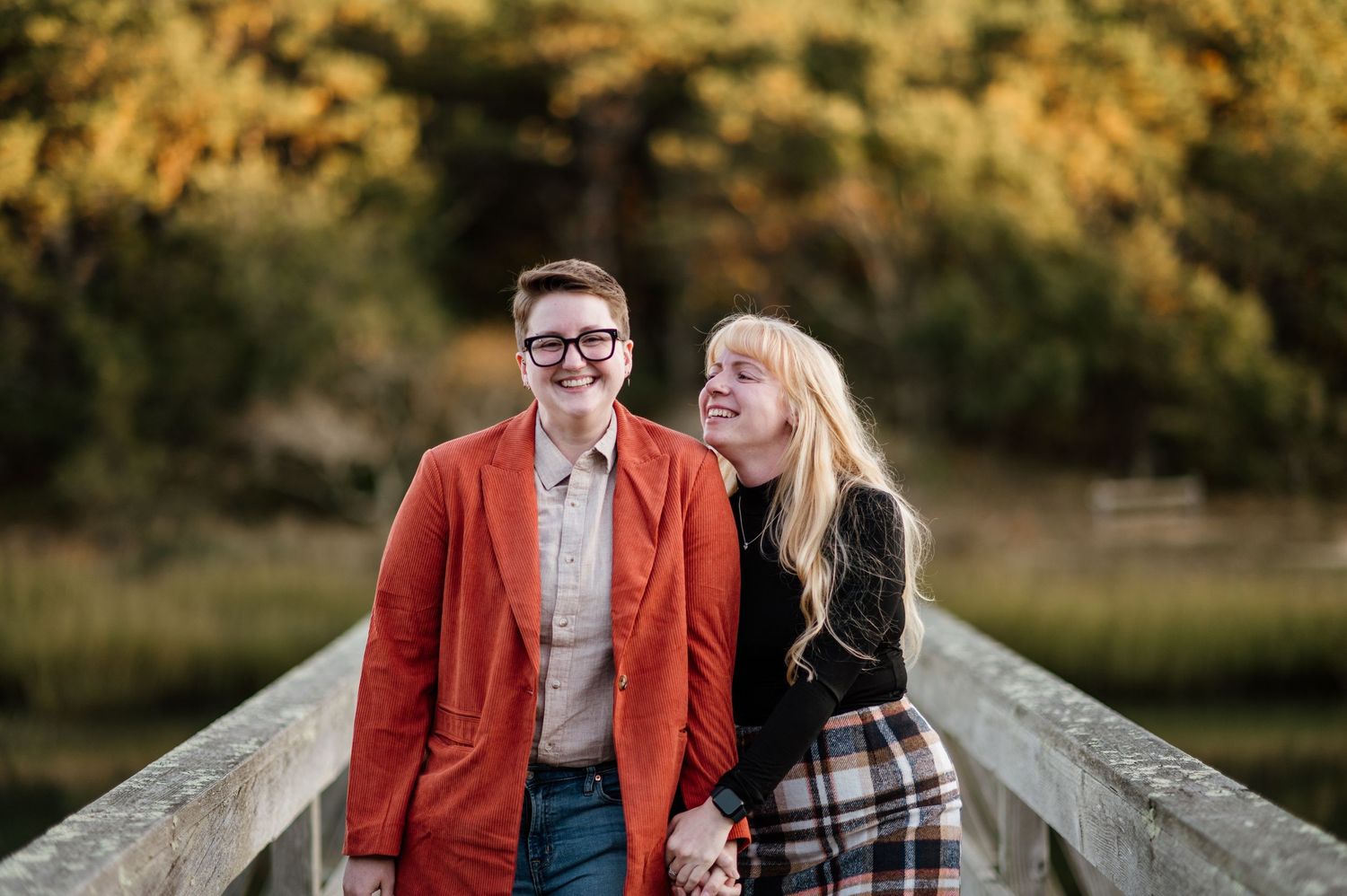 A romantic couple poses together on a wooden bridge during golden hour in autumn.