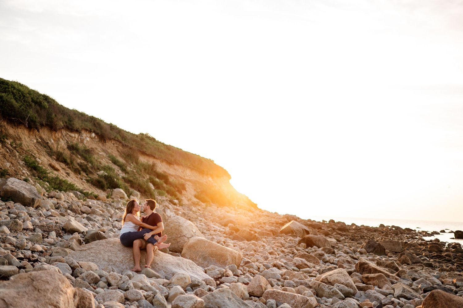 Couple walking along rocky coastal cliffs during golden hour with ocean views.