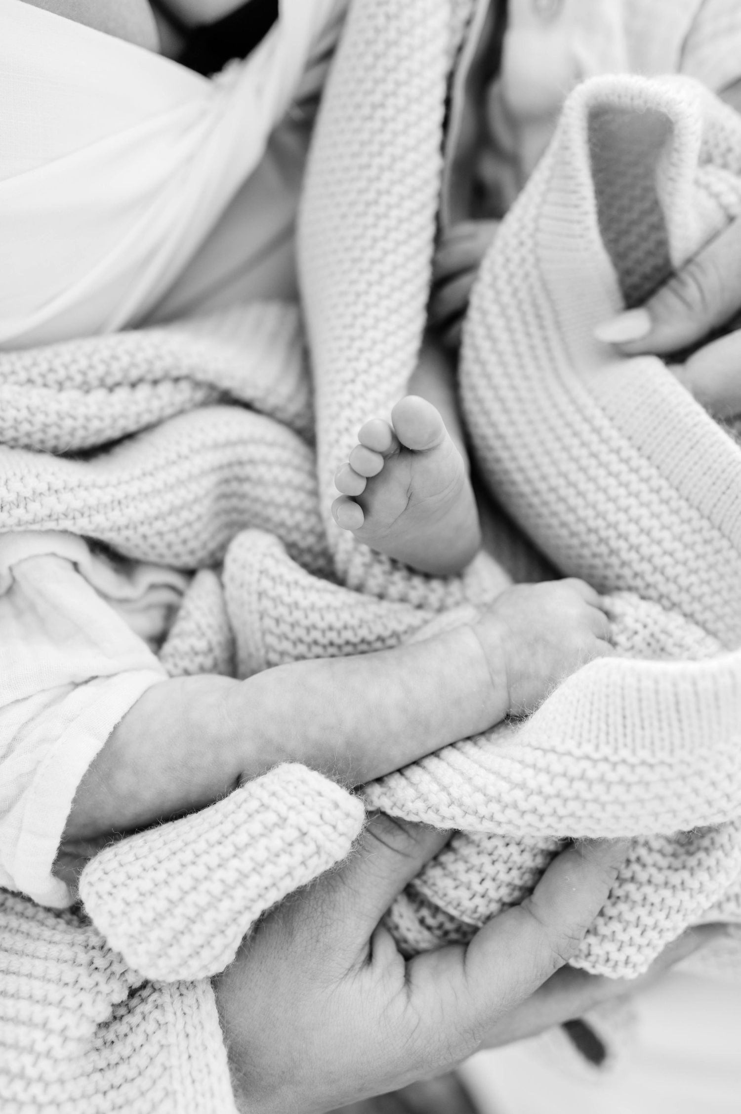 Close-up black and white images of tiny baby feet wrapped in a knitted white blanket.