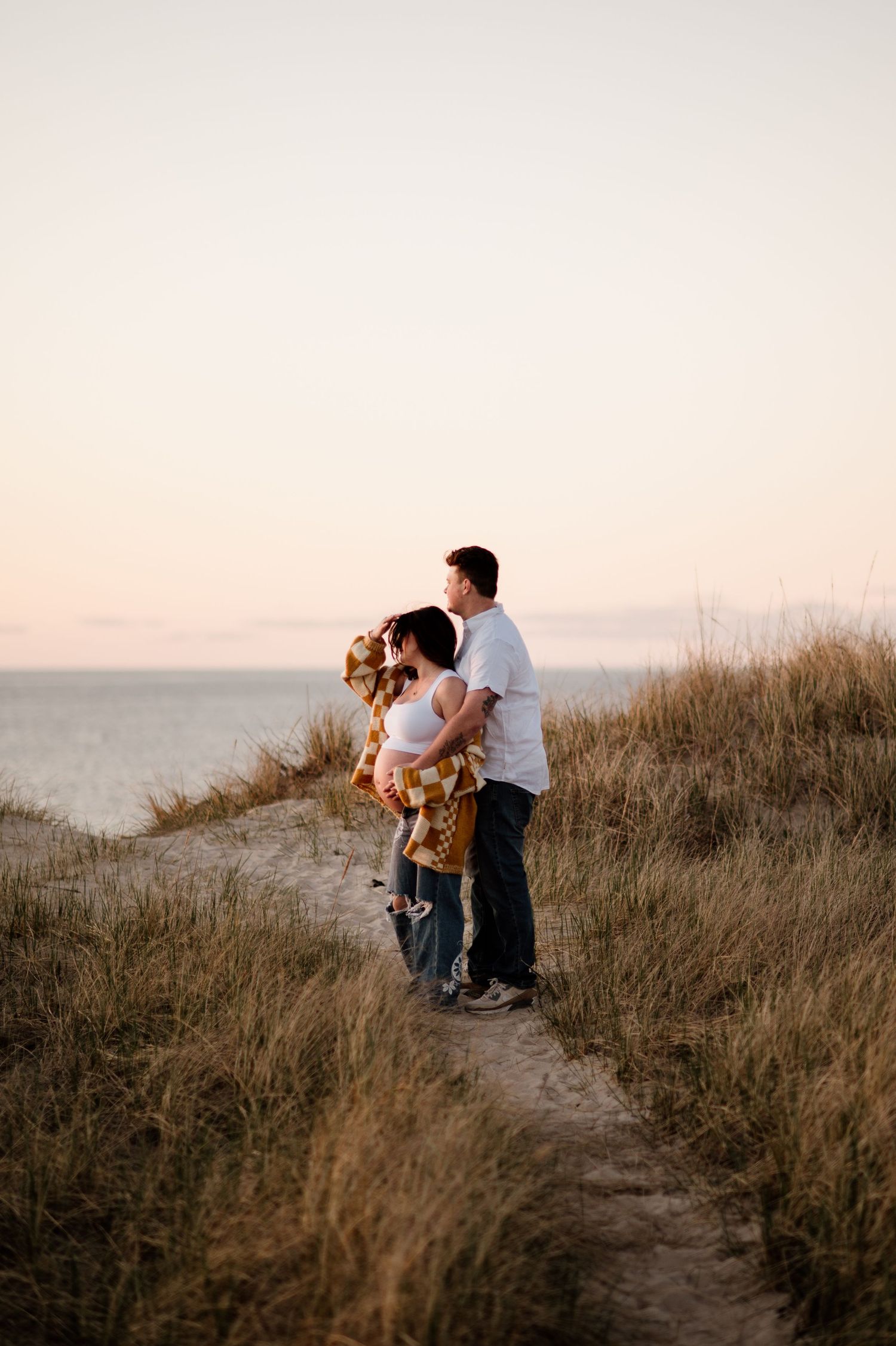 Family silhouettes against sunset sky on coastal path with tall grass.