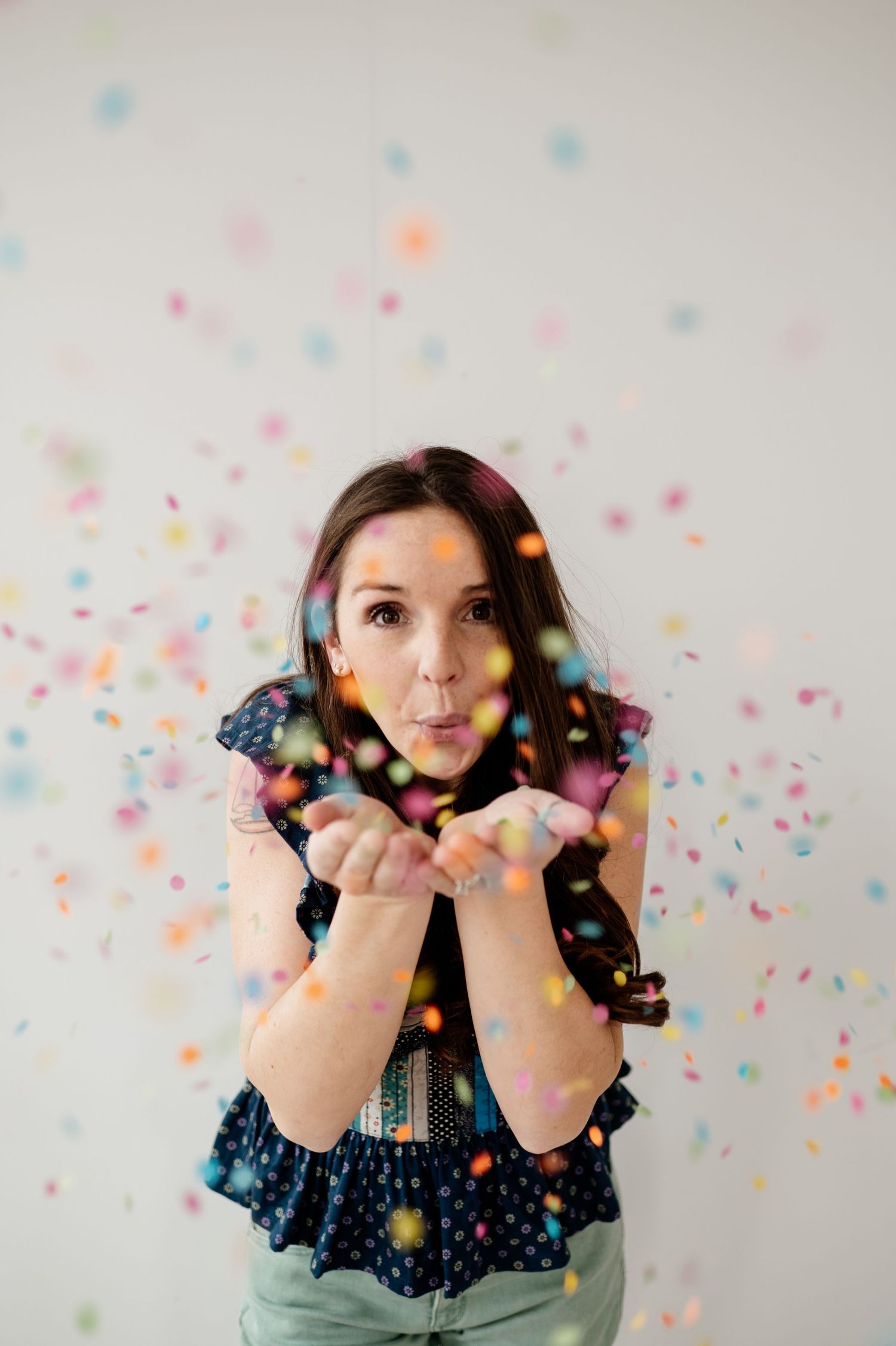 A playful portrait with colorful confetti being blown against a light background.
