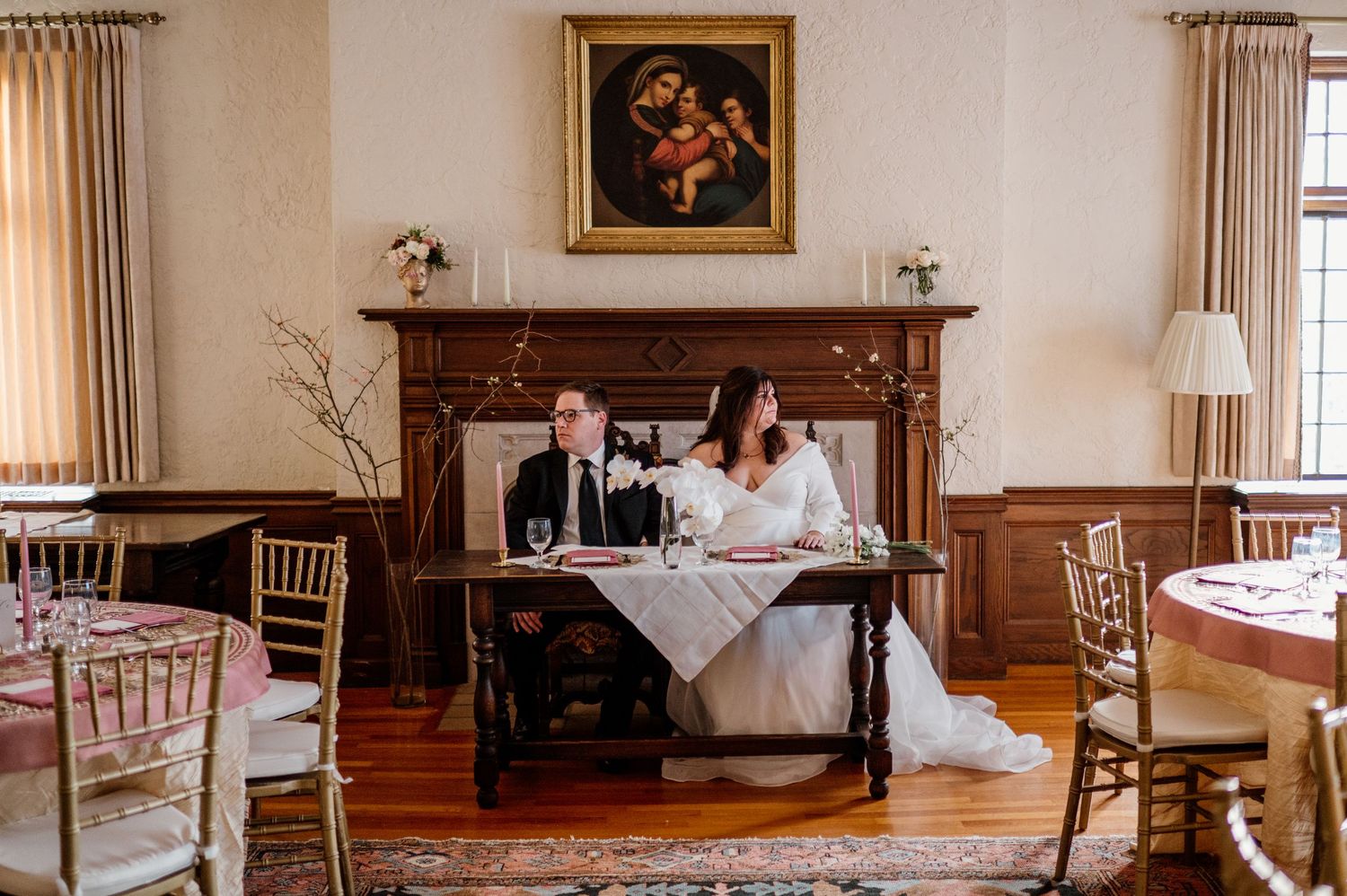 A couple sits at an elegant wooden desk in a reception room with wood paneling and vintage decor.