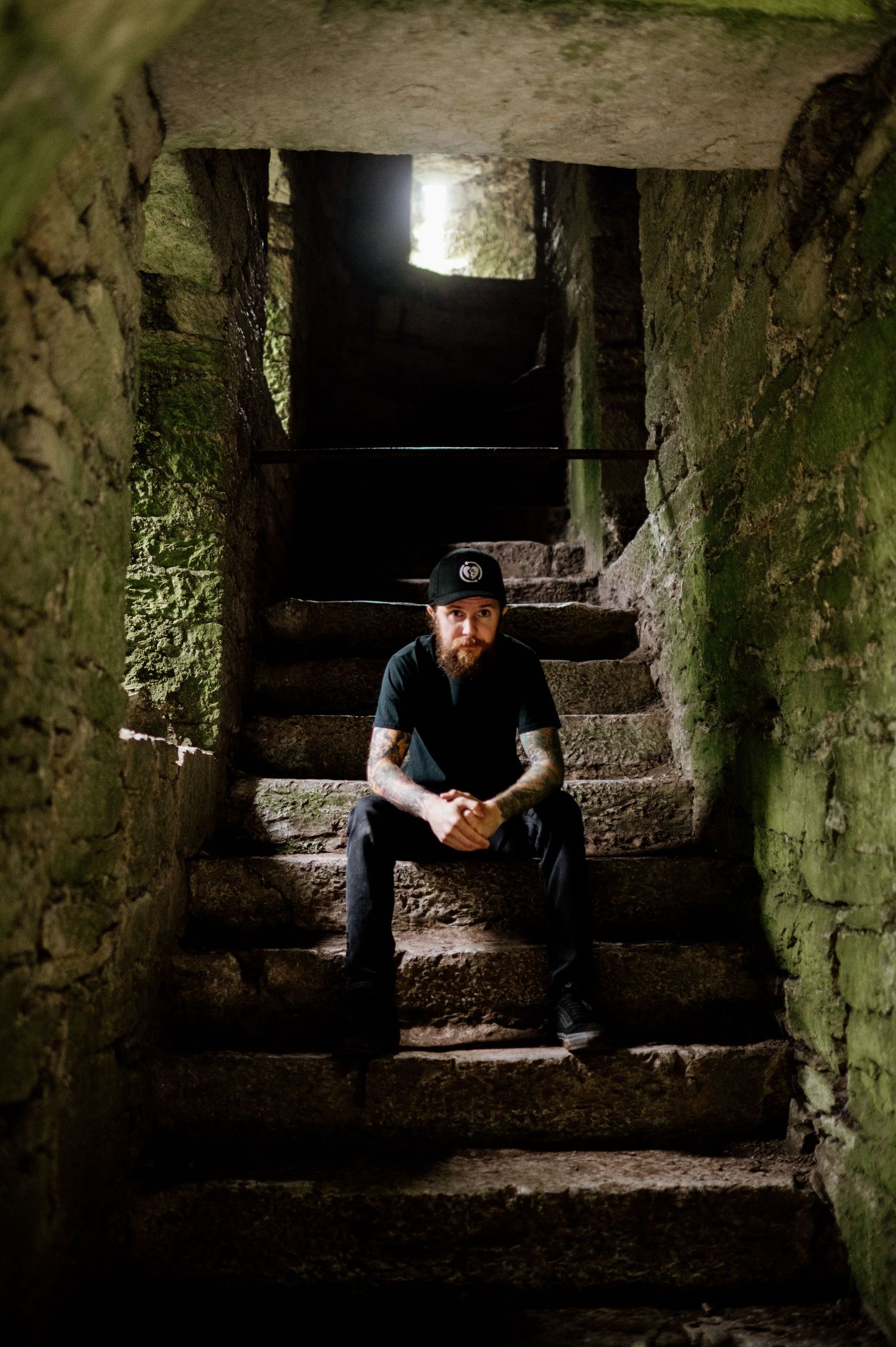 A series of dark stone steps in an ancient underground tunnel or crypt illuminated by dim natural light.