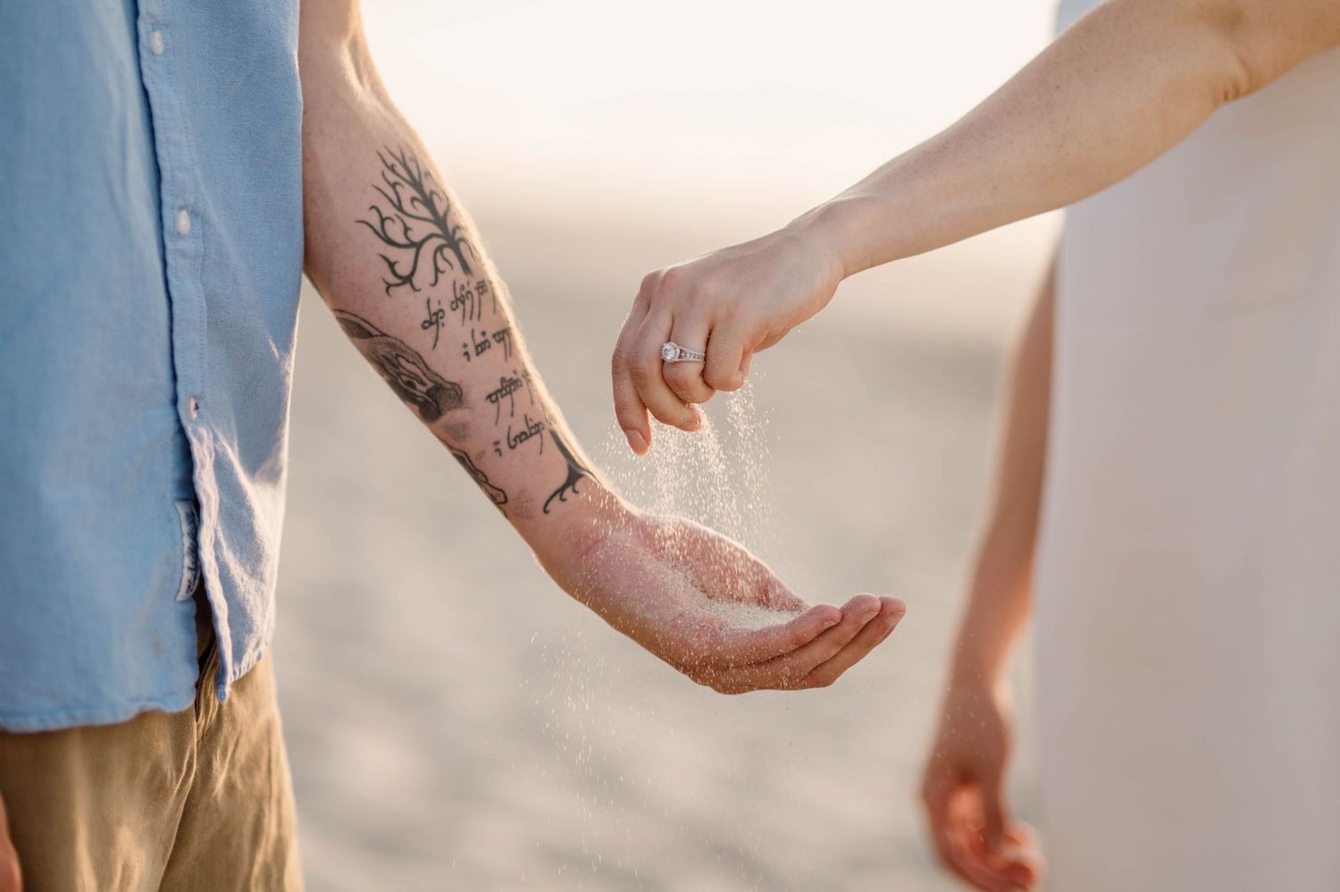 Close up of hands reaching toward each other with delicate tattoo details.