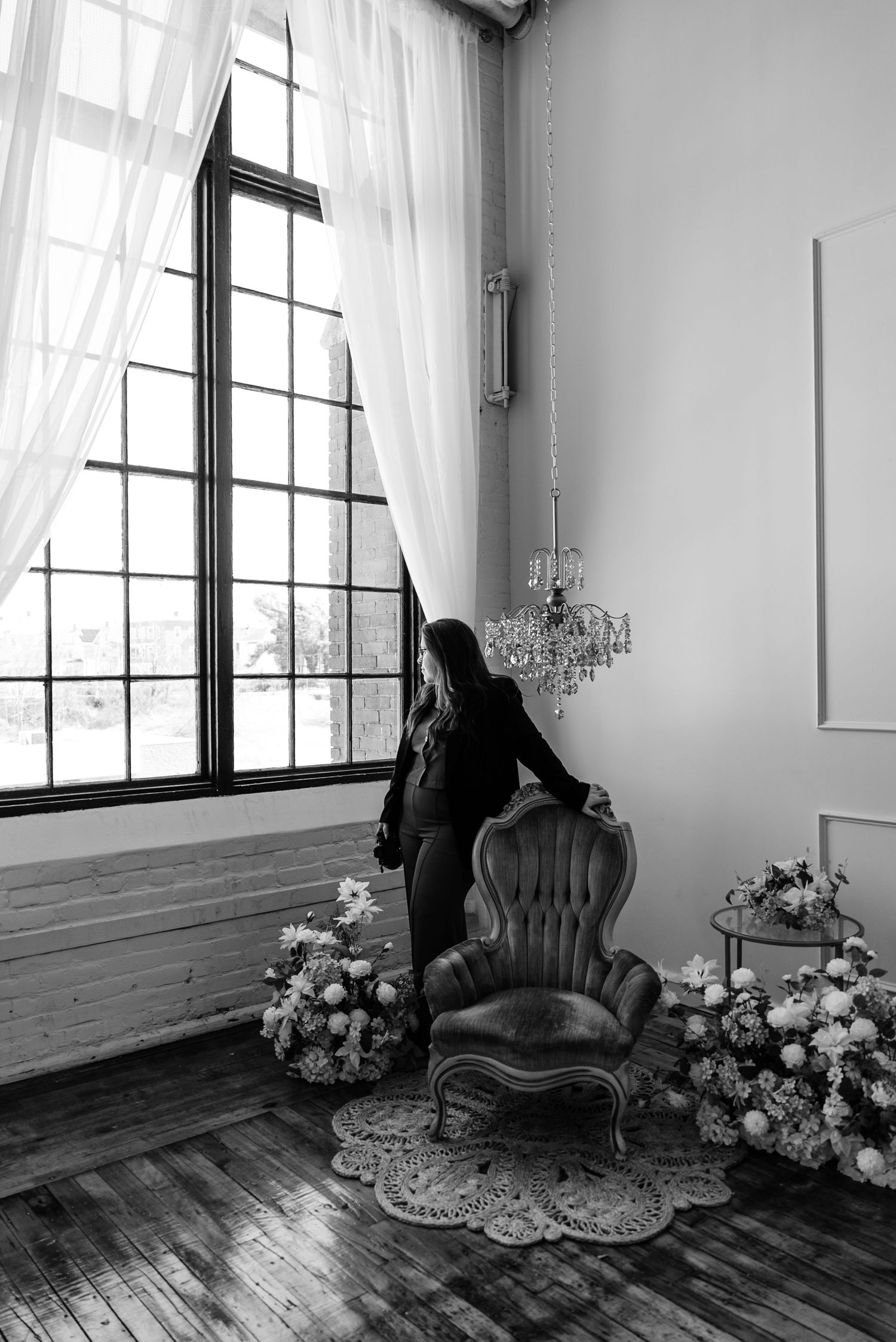 Elegant vintage armchair with floral arrangements and chandelier in a bright white studio with large windows.