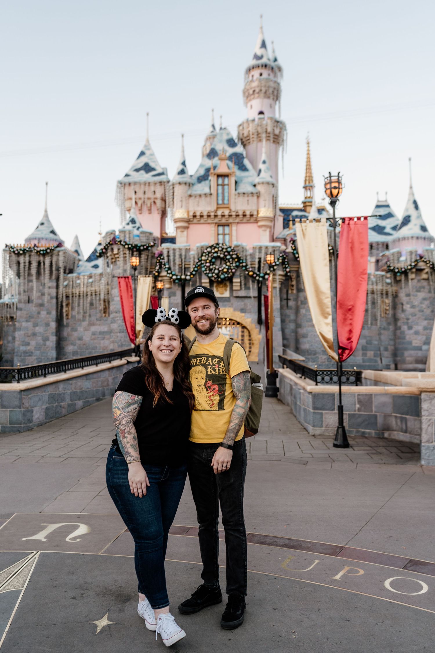 A couple poses together in front of Sleeping Beauty Castle at Disneyland theme park during different moments of their visit.