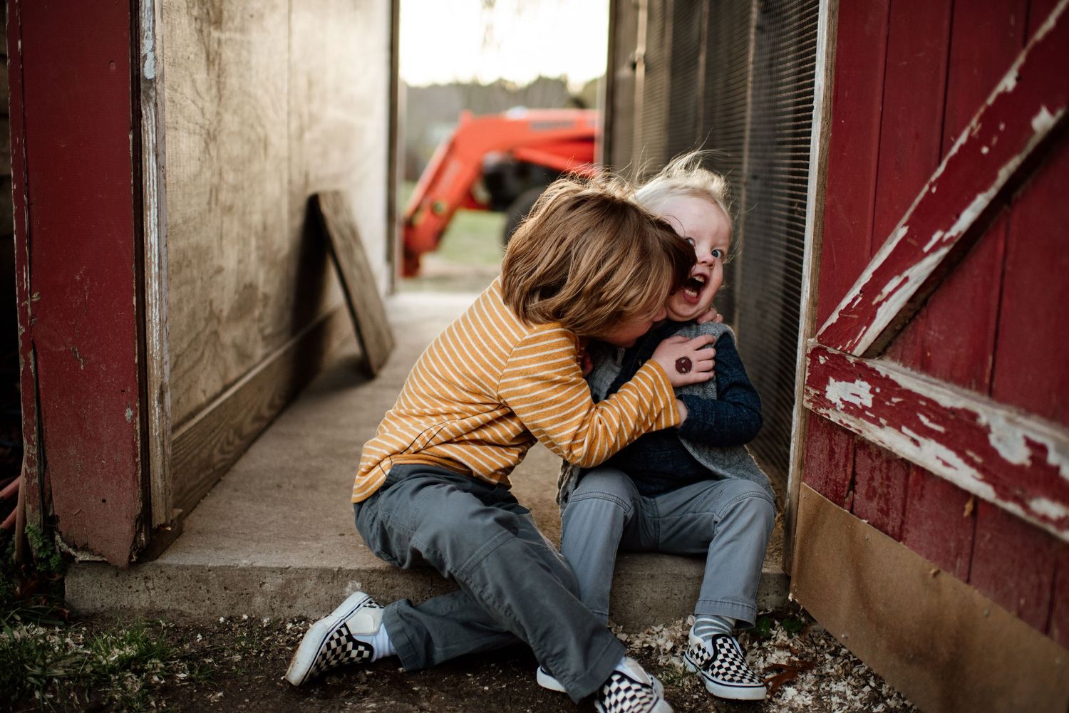 Two people sit close together near a rustic red barn door.