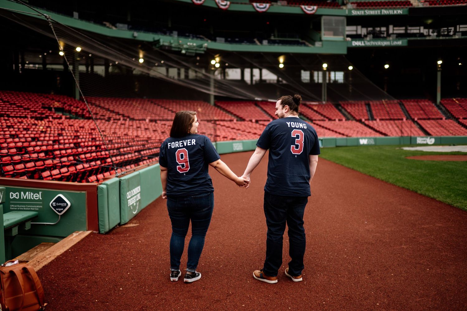 Two people in matching outfits walk along empty red stadium seats at a baseball field.