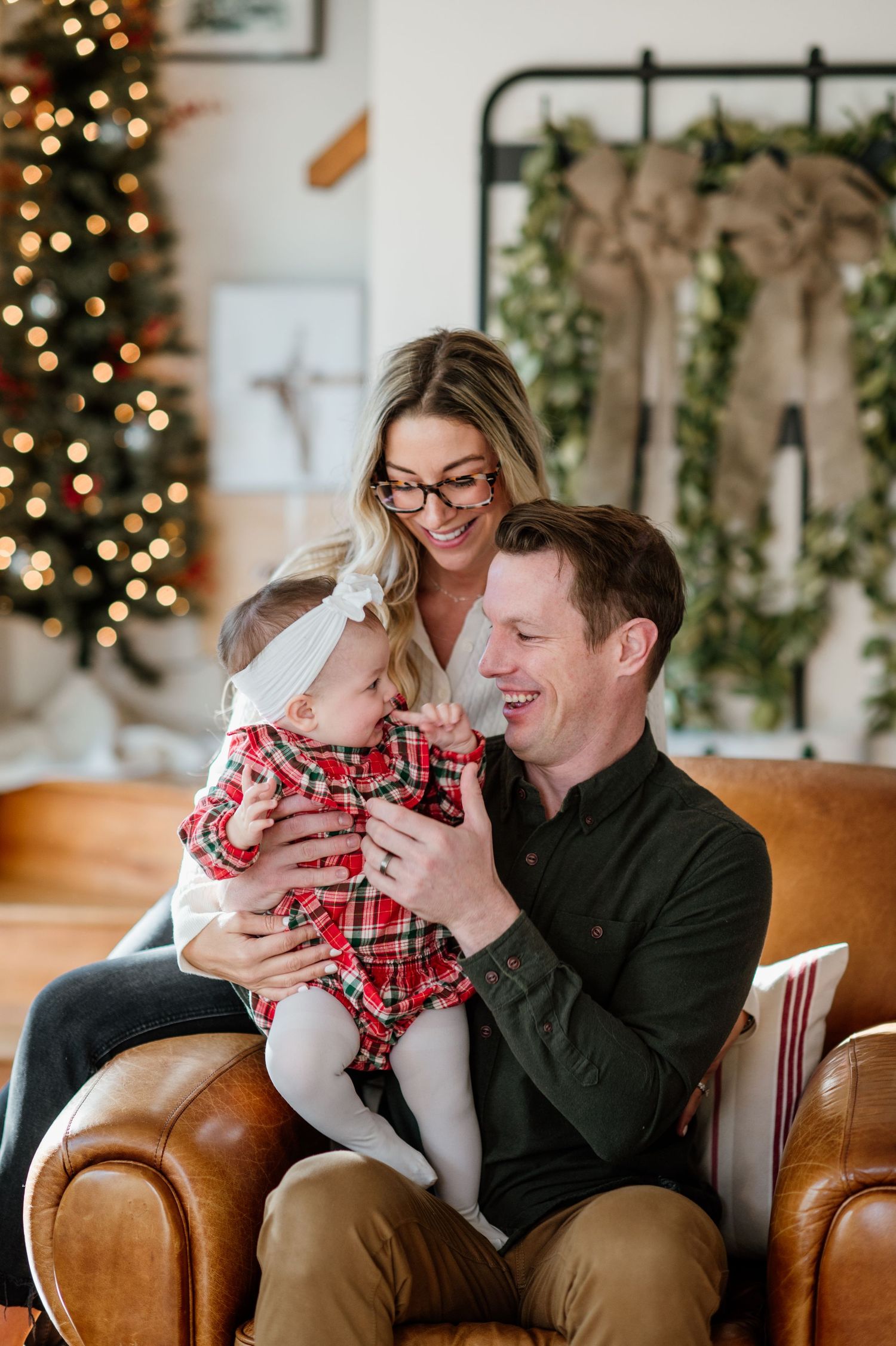 Cozy family moment on brown leather couch with Christmas decorations and twinkling lights in background.