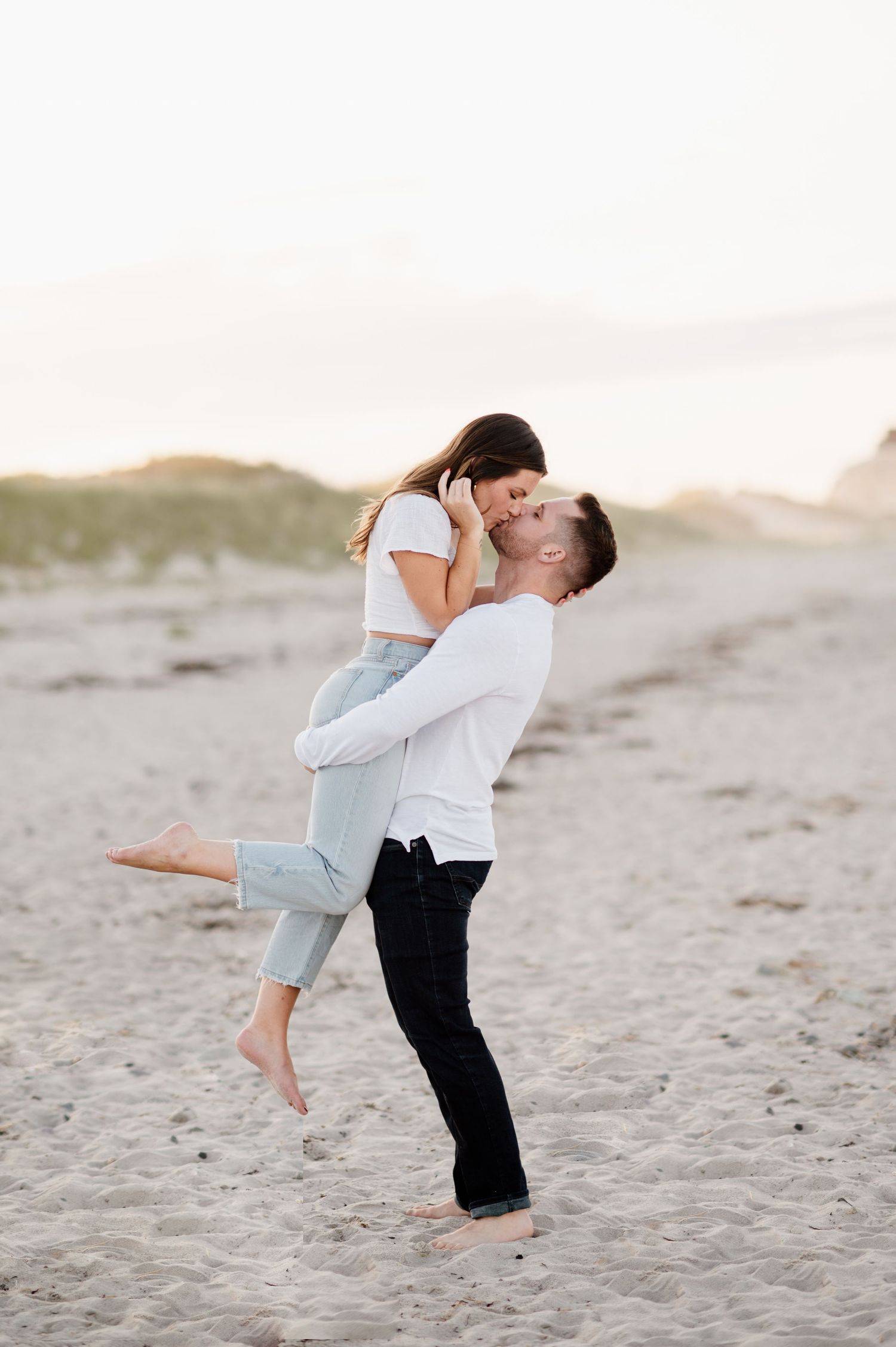 A couple embraces and shares a romantic moment while dancing on a sandy beach at sunset.