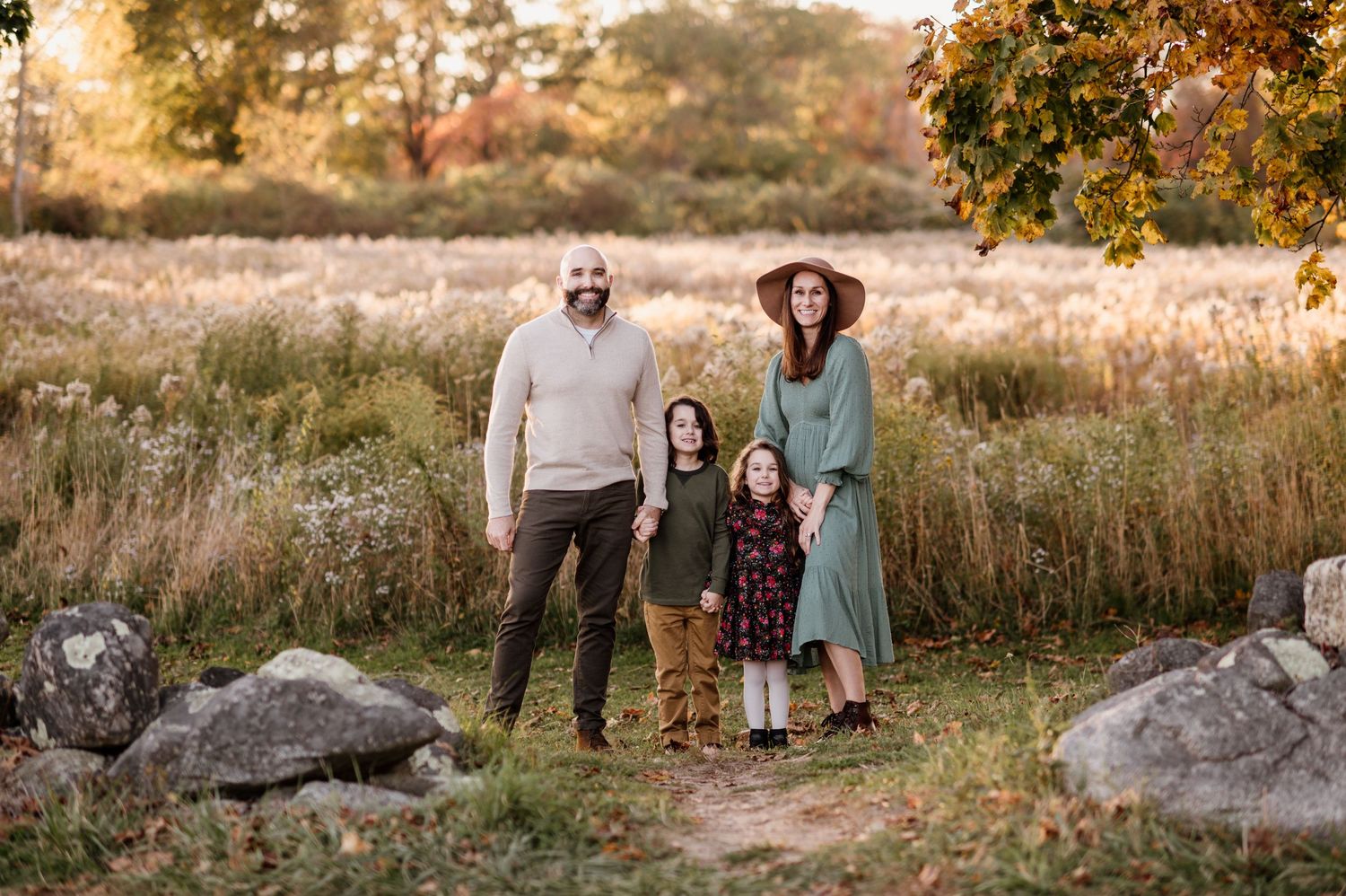 A group poses together in a golden autumn field during sunset with warm fall colors in the background.