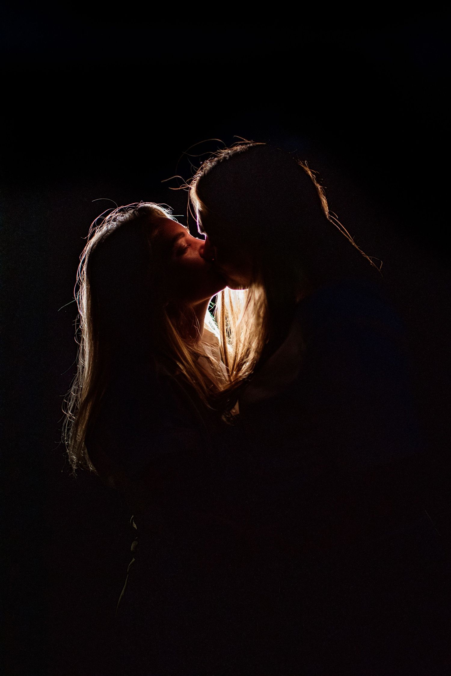 Silhouetted figures in dramatic backlit pose against dark background with rim lighting.