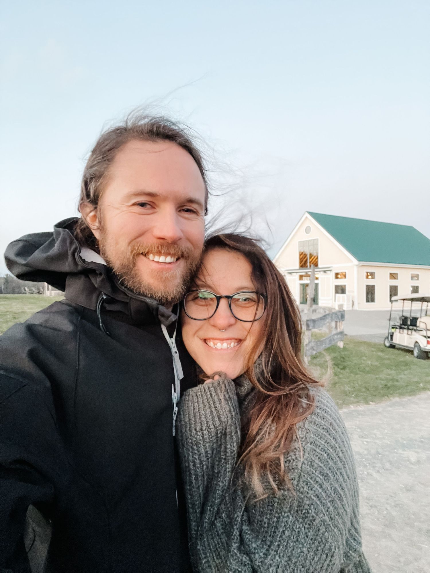 A couple shares a joyful moment together outdoors with rural buildings visible in the background.