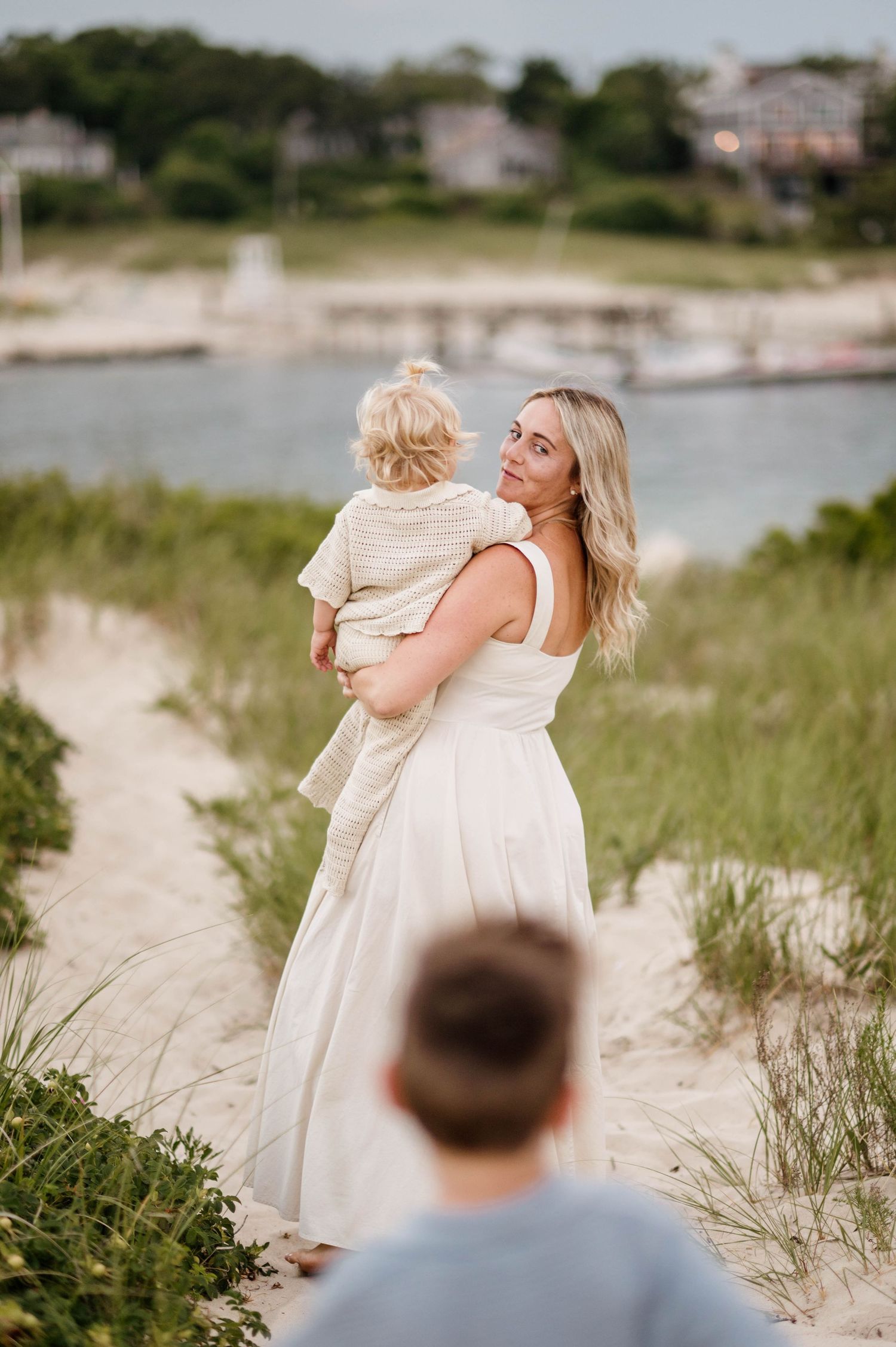 Candid beach photoshoot with family in white and blue outfits against coastal backdrop.