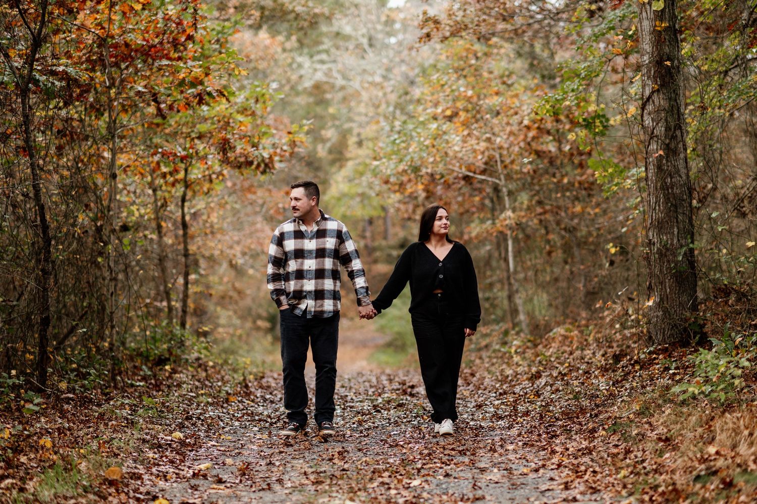 Autumn engagement photo session with fallen leaves covering a wooded trail.