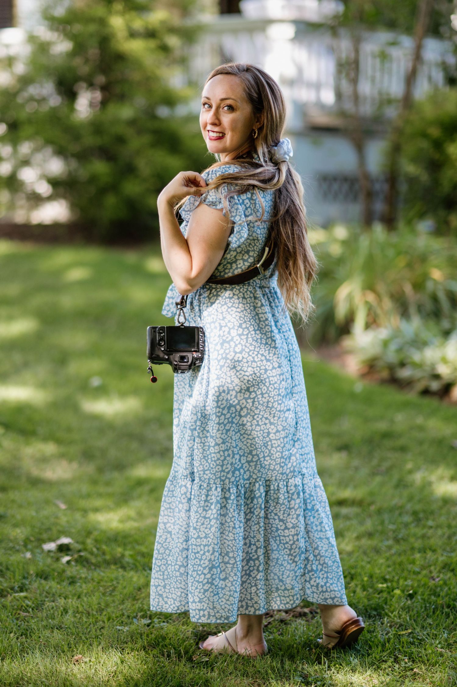 A person in a light blue floral maxi dress poses in a garden setting while carrying a small black handbag.