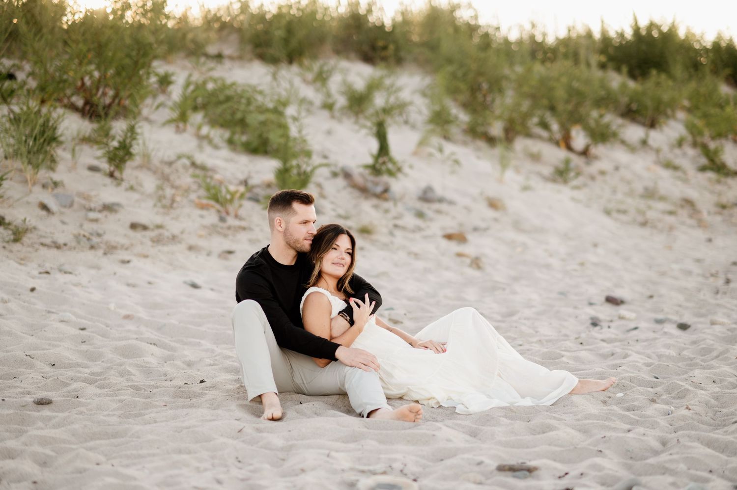 A couple in formal attire shares a romantic moment together on a sandy beach at sunset.