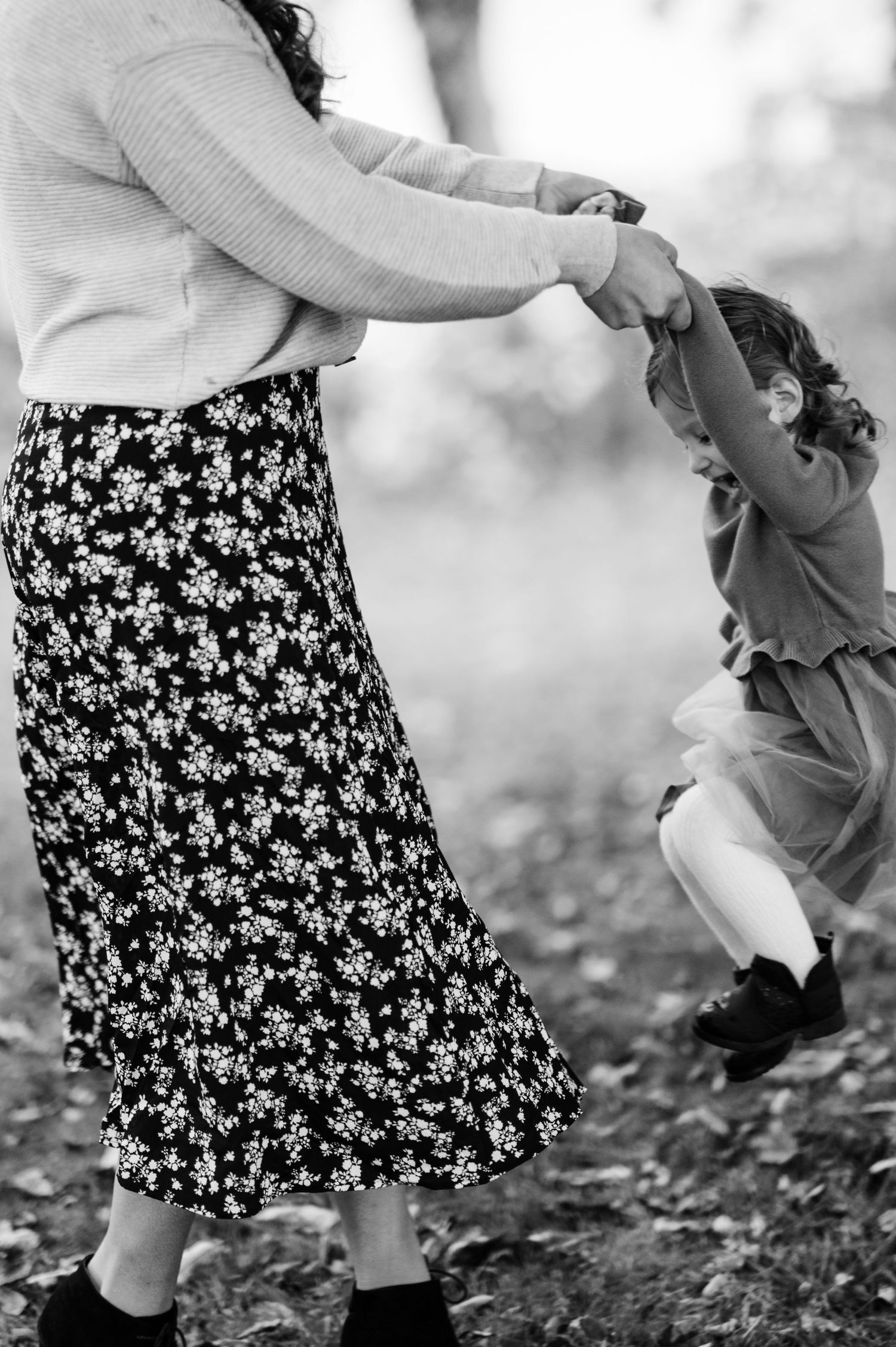 Black and white close-up of someone wearing a floral patterned skirt walking through fallen leaves.