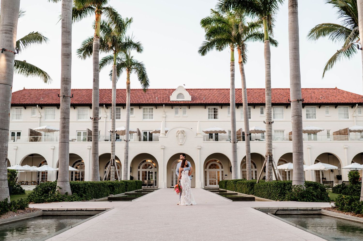 Spanish colonial architecture with palm trees lines a pathway at an elegant resort entrance.