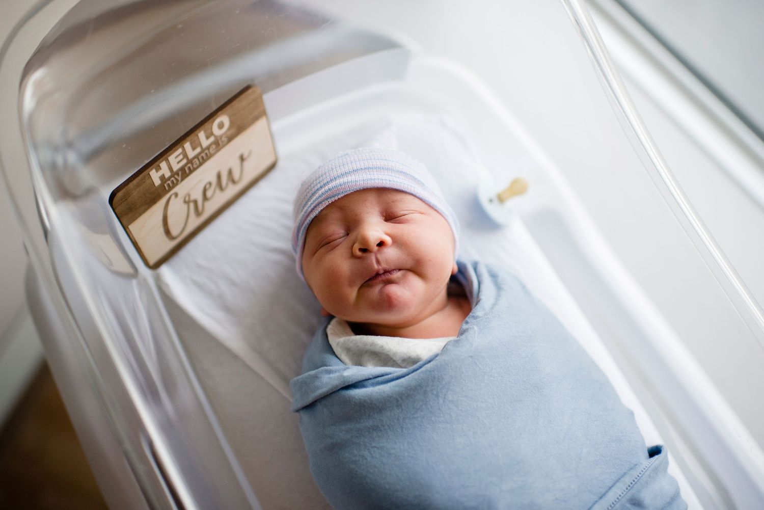 Newborn baby sleeping peacefully swaddled in blue blanket with hospital identification.