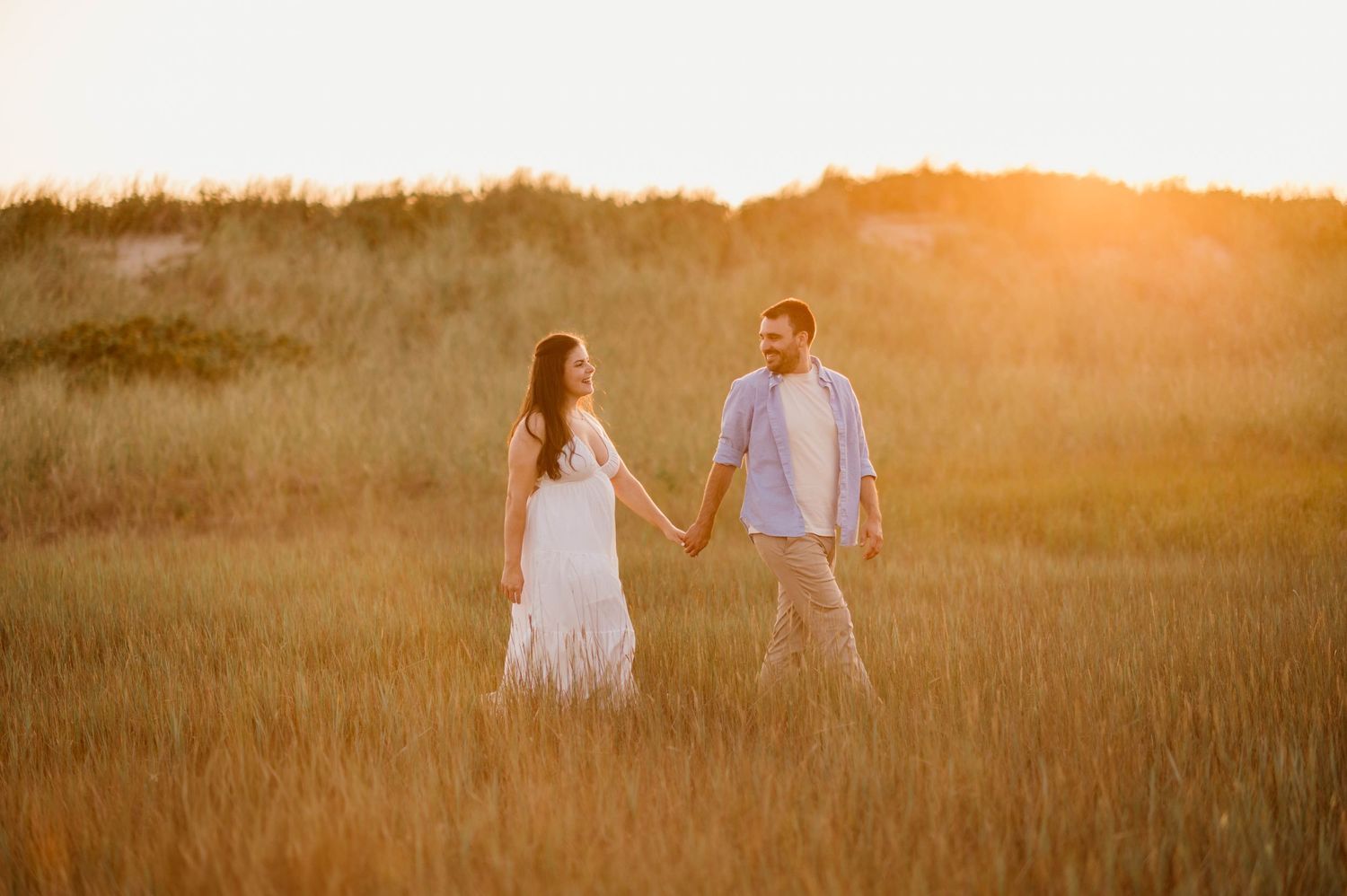 Couple walking through golden field at sunset with warm glowing light.