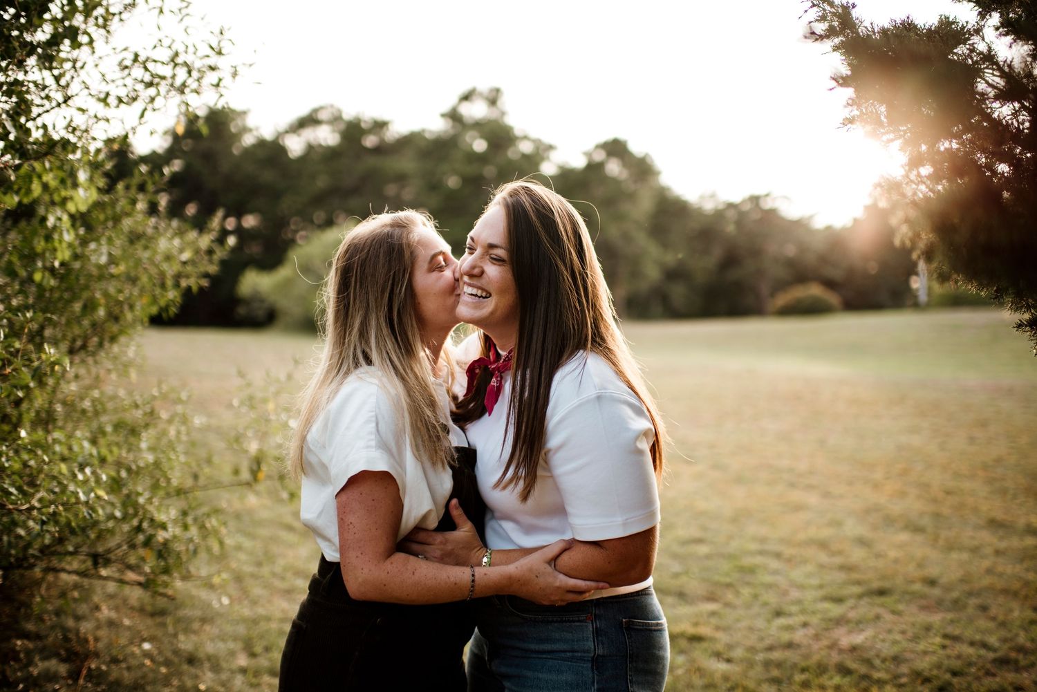 Two friends share laughter and embrace in a sunlit field during golden hour.