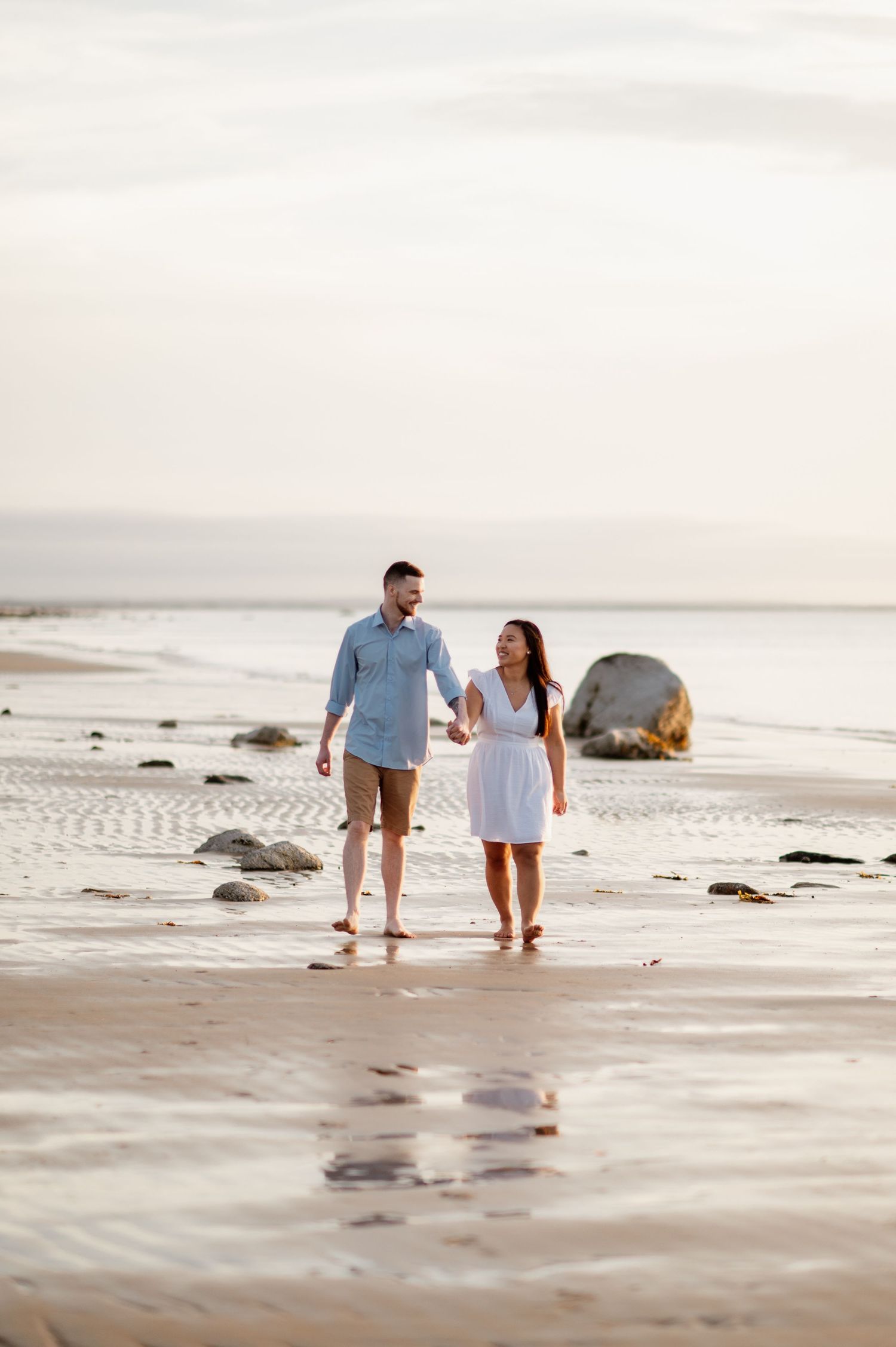 A couple takes a romantic stroll along a rocky beach at sunset.