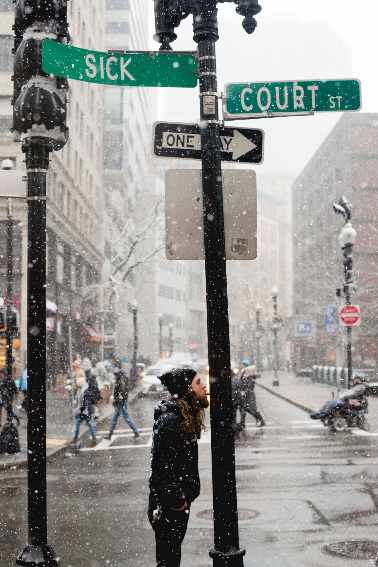 Street sign intersection of Sick Street and Court Street during snowy winter weather in a city.