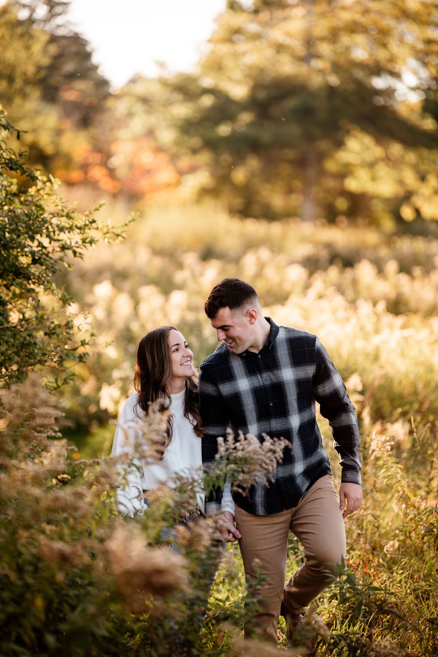 A couple shares tender moments in a sunlit field with golden autumn foliage.