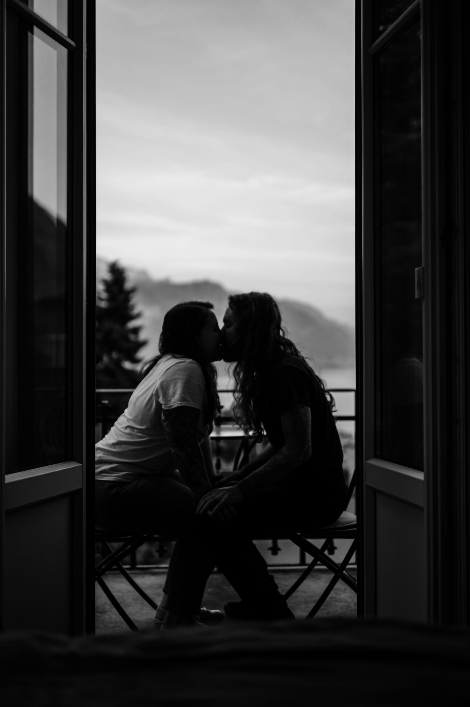 Silhouettes of people sitting by open windows at sunset creating a moody black and white composition.