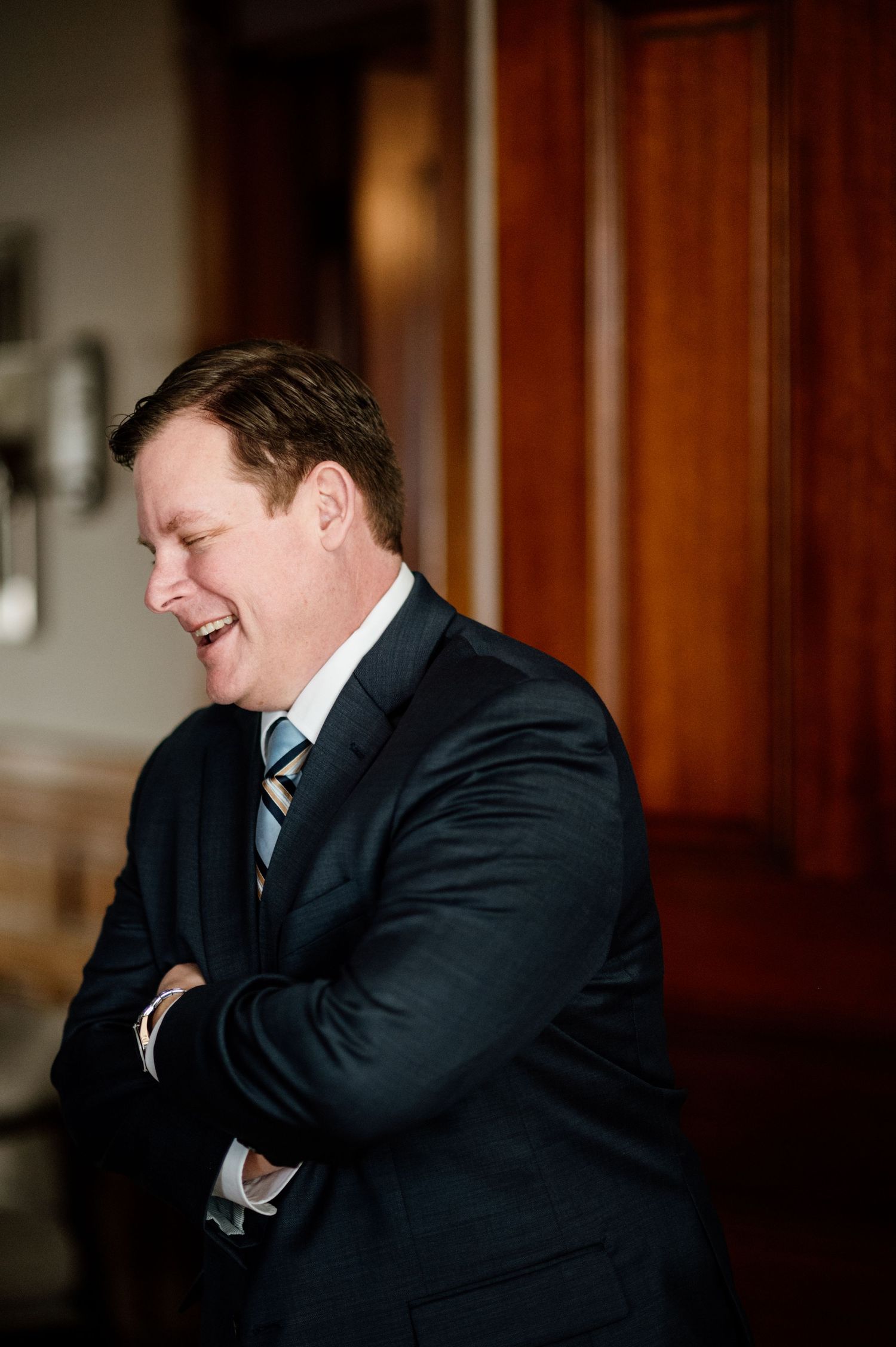 A sequence of candid photos showing hearty laughter in black suit against wood paneling.